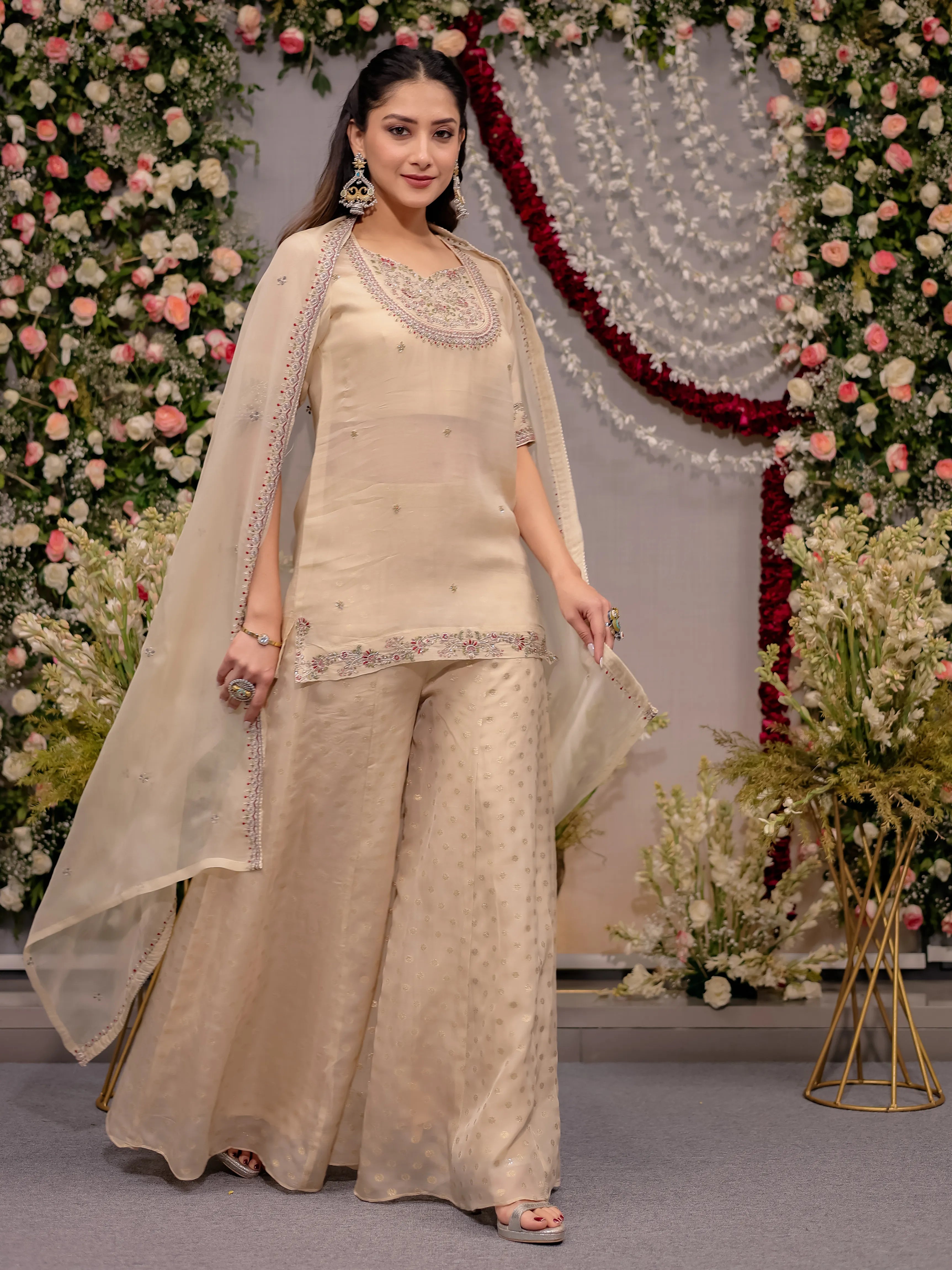 Woman in a beige traditional outfit with floral decorations in the background