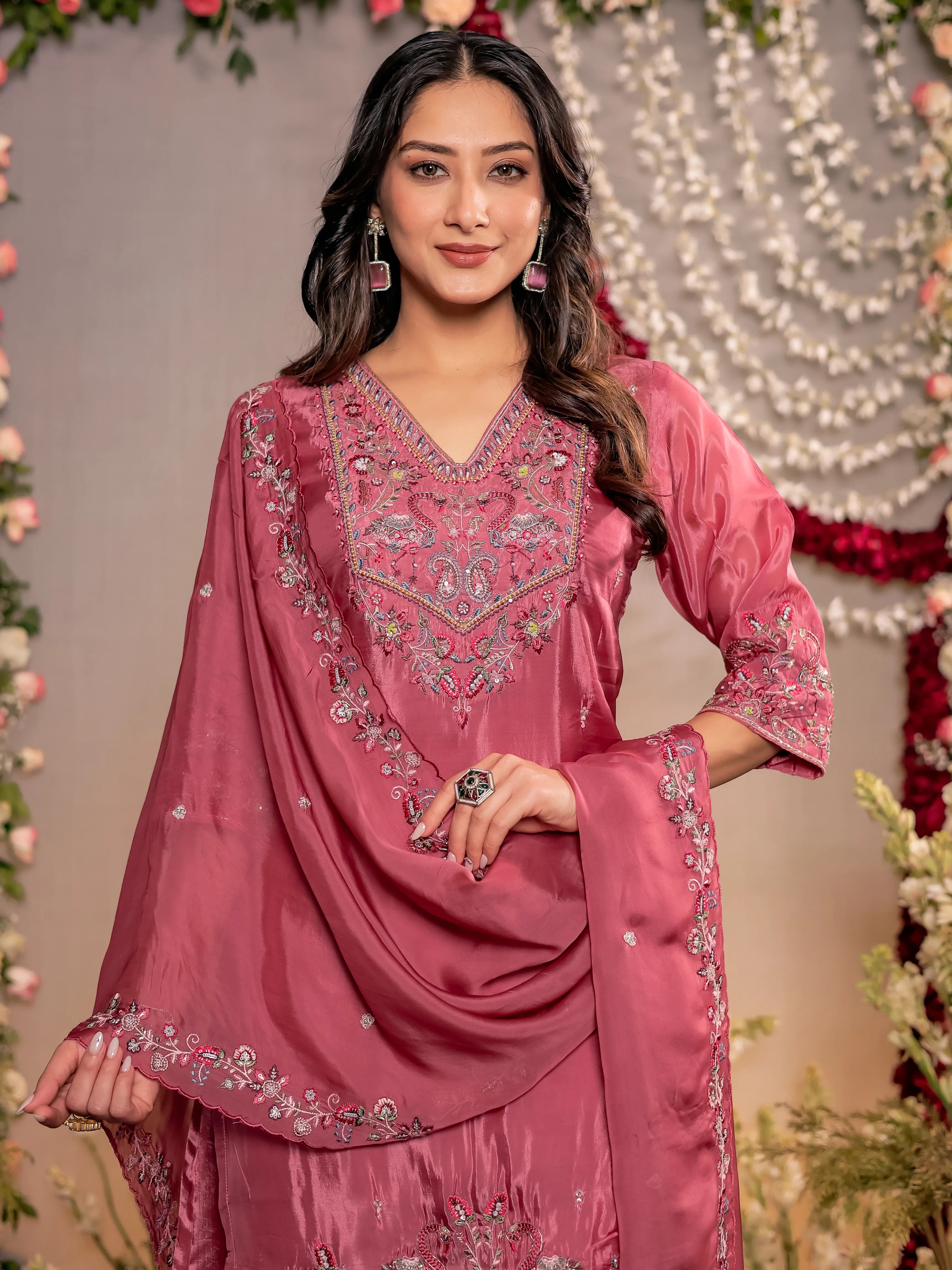 Woman wearing a pink embroidered traditional outfit with a decorative background