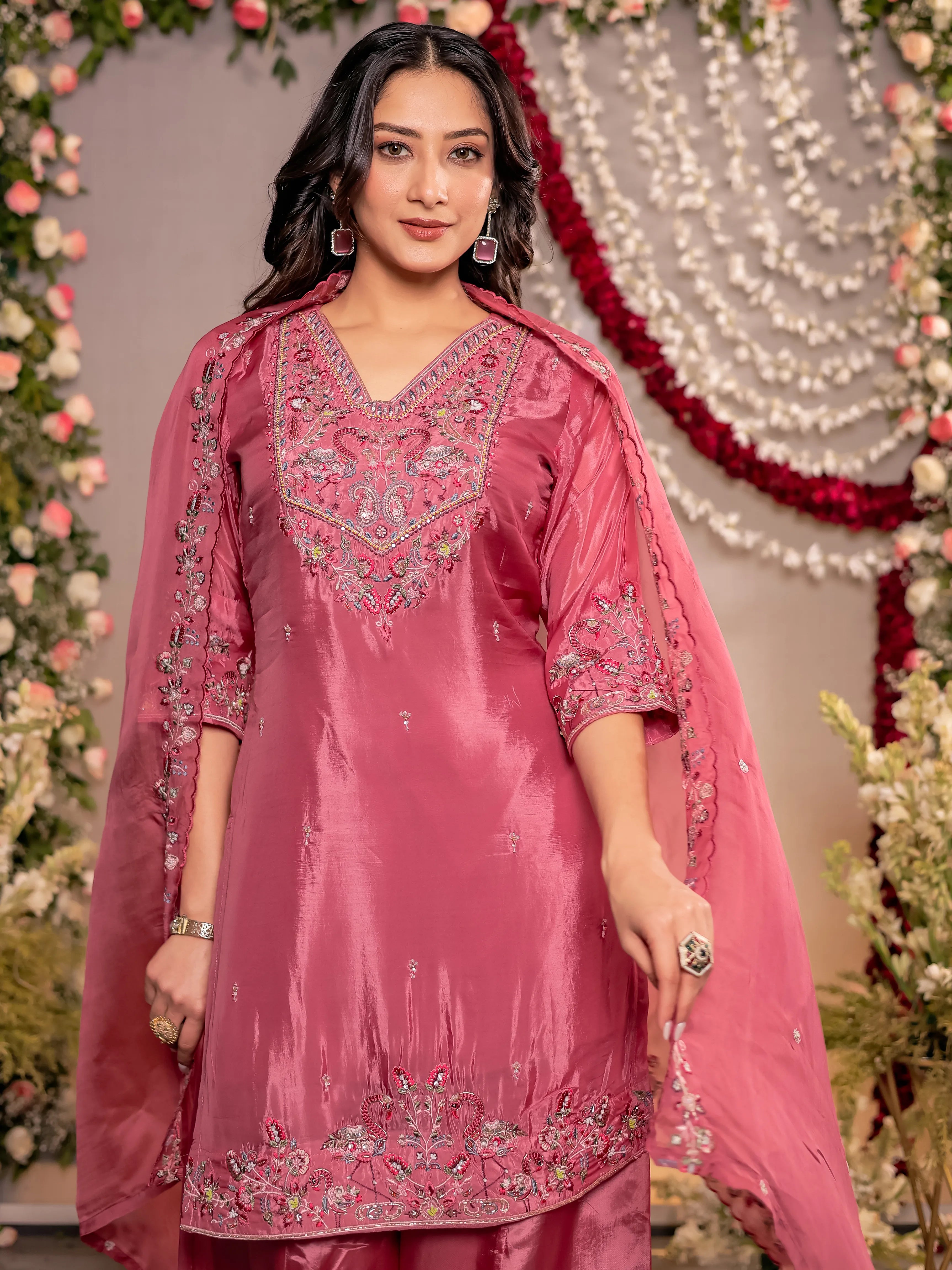 Woman wearing a pink embroidered traditional outfit with a decorative background
