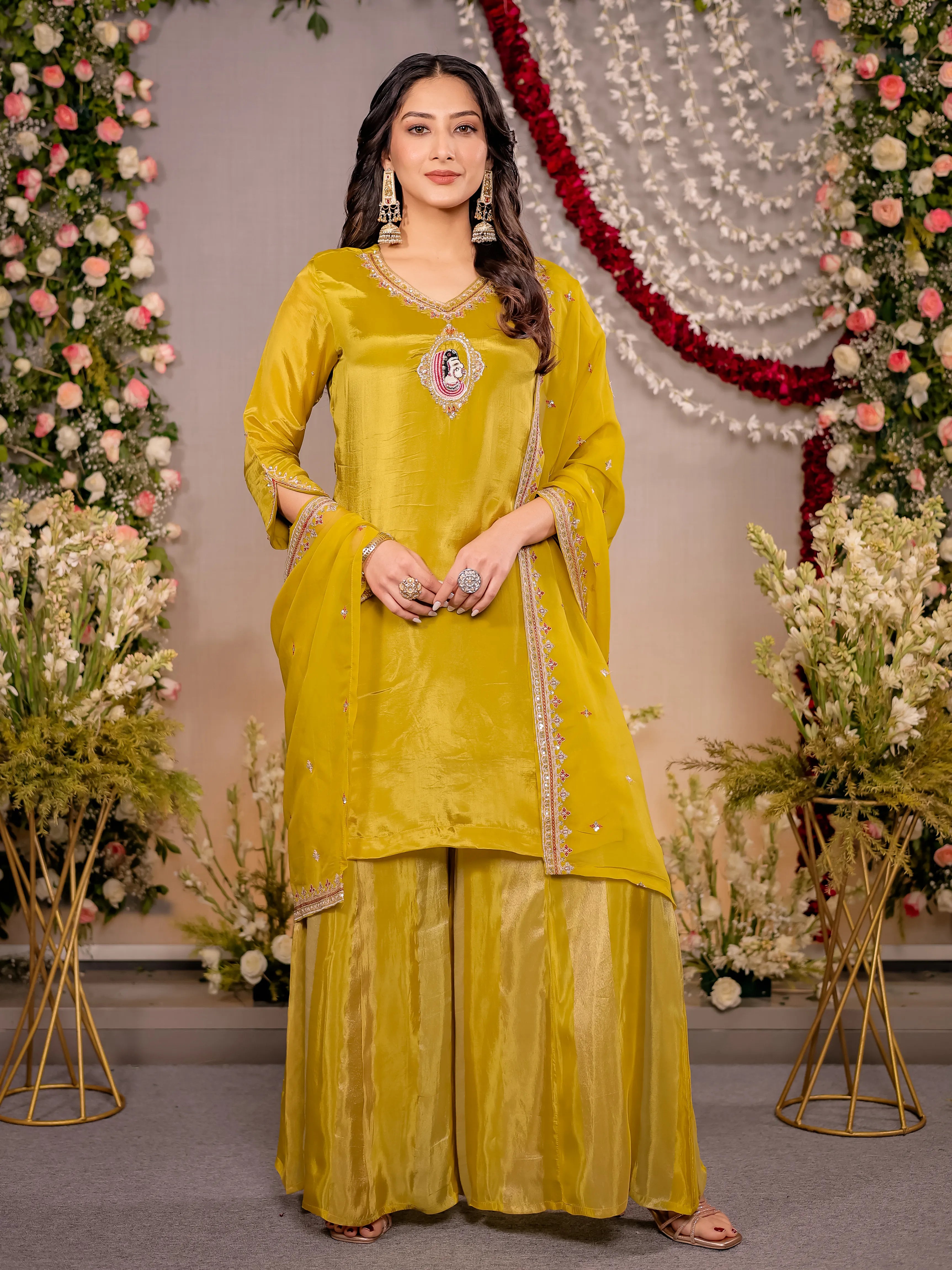 Woman in a yellow traditional outfit standing in front of floral decorations