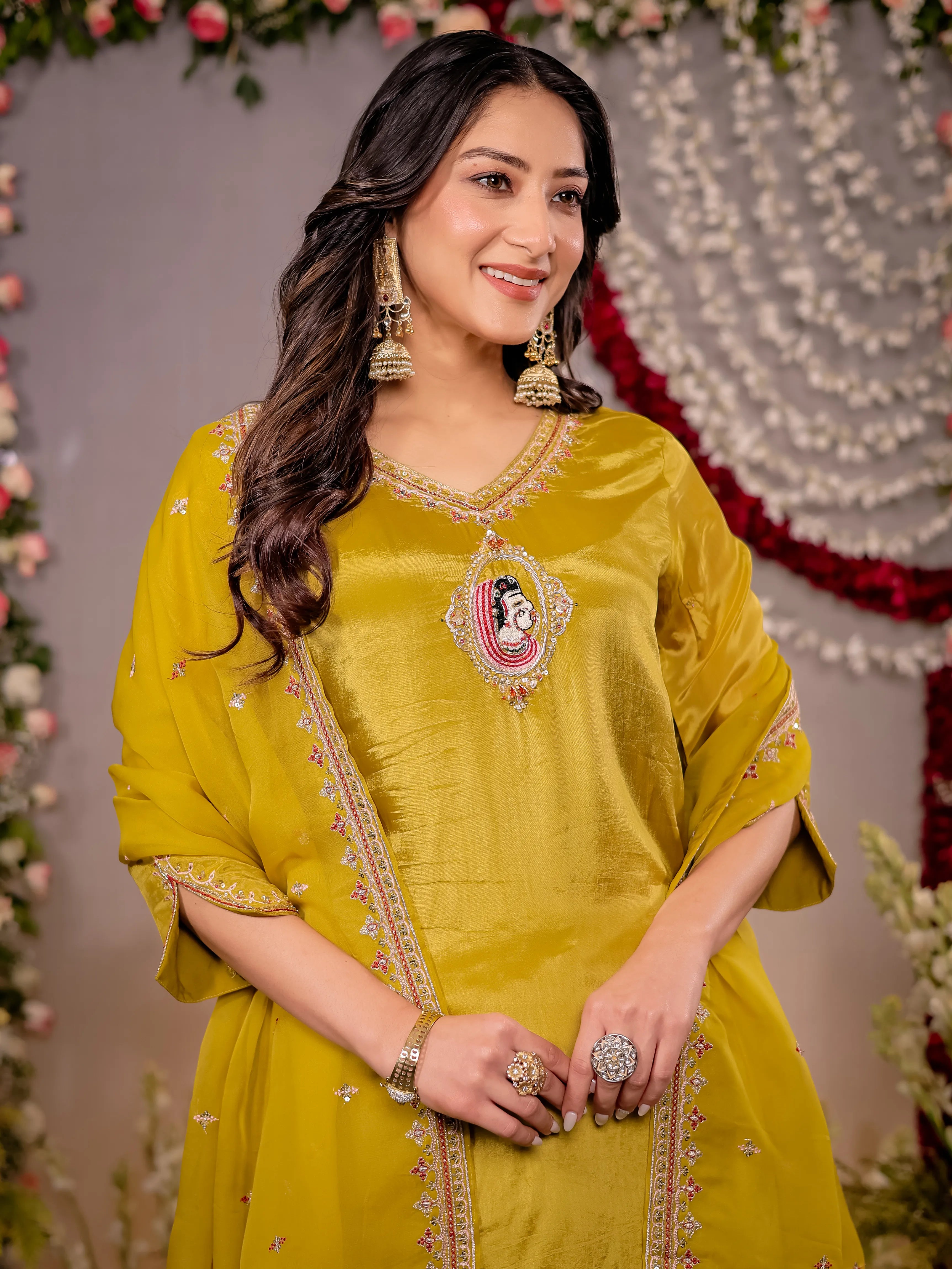 Woman in a yellow traditional outfit with jewelry against a decorated background
