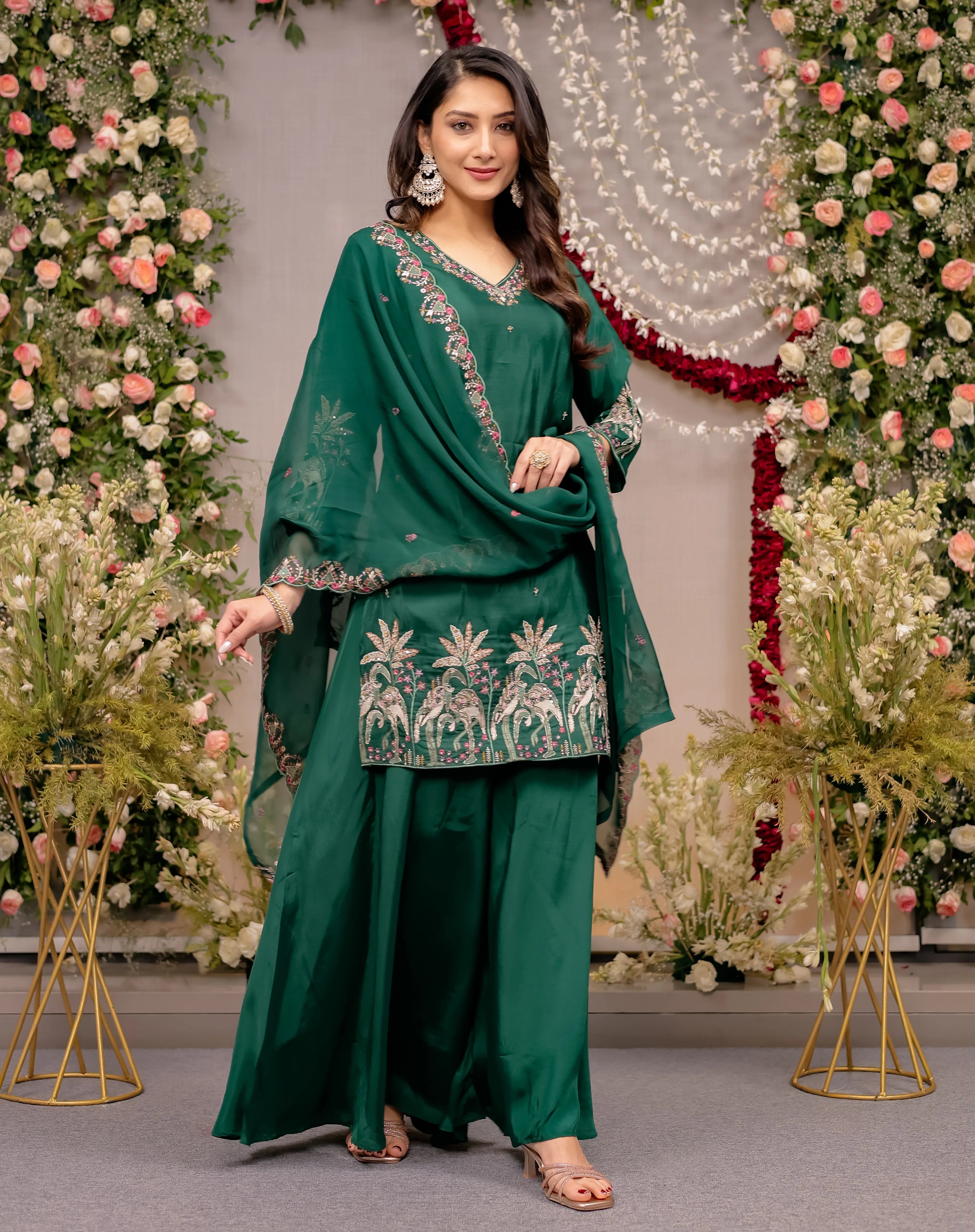 Woman in a green traditional outfit with floral patterns against a decorated background