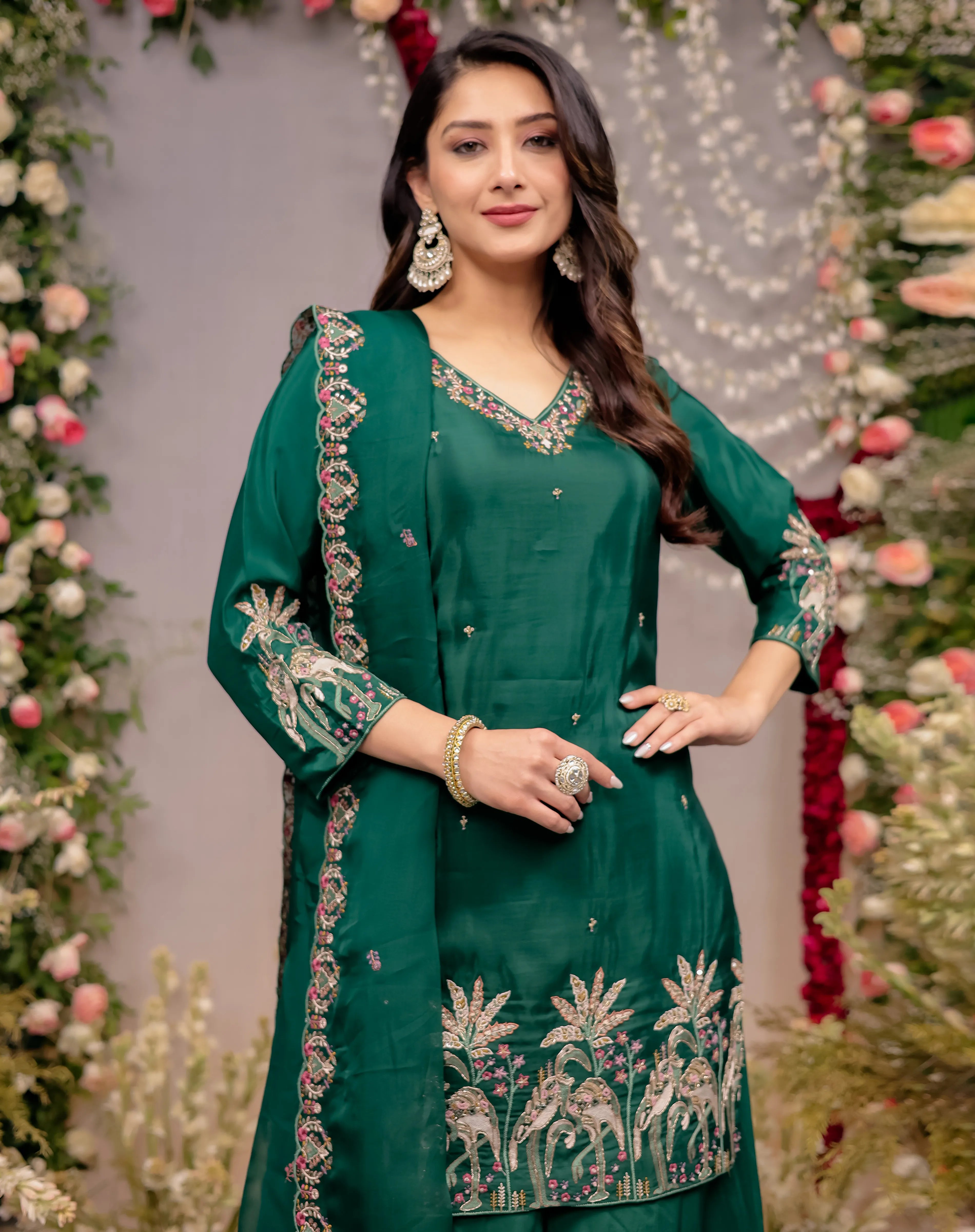 Woman in a green embroidered outfit standing in front of floral decorations