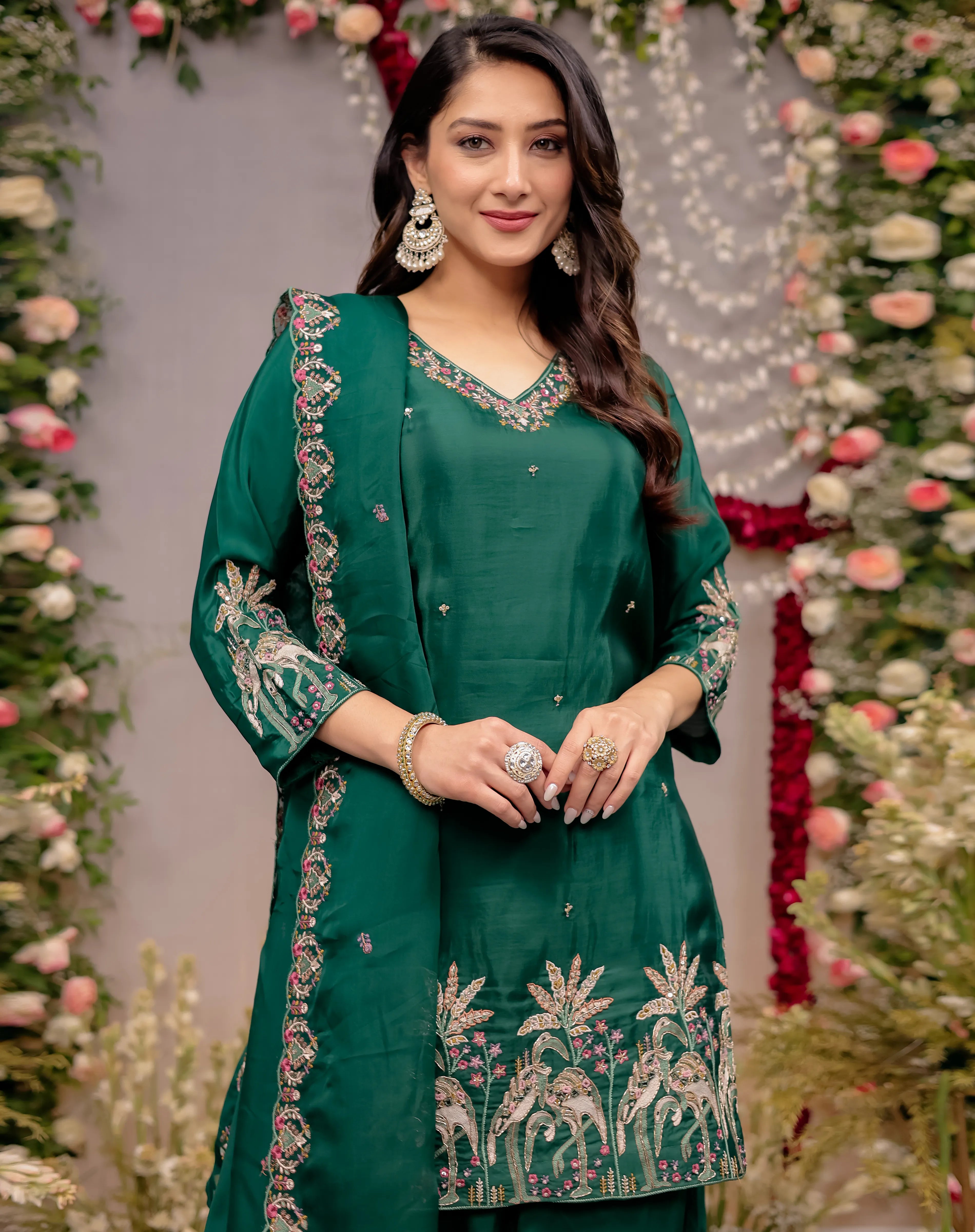 Woman in a green embroidered outfit standing in front of floral decorations