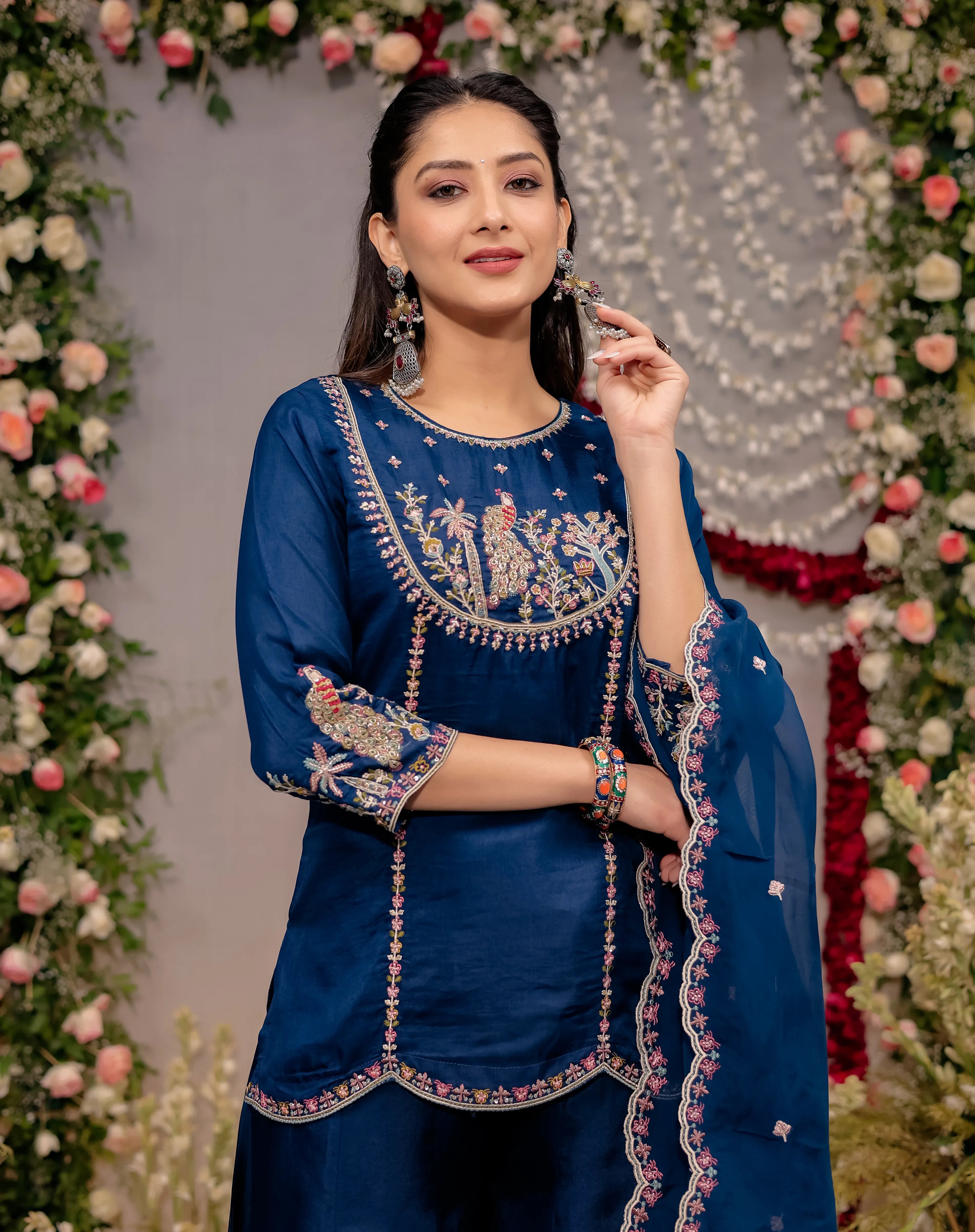 Woman in a blue embroidered traditional outfit with floral decorations in the background
