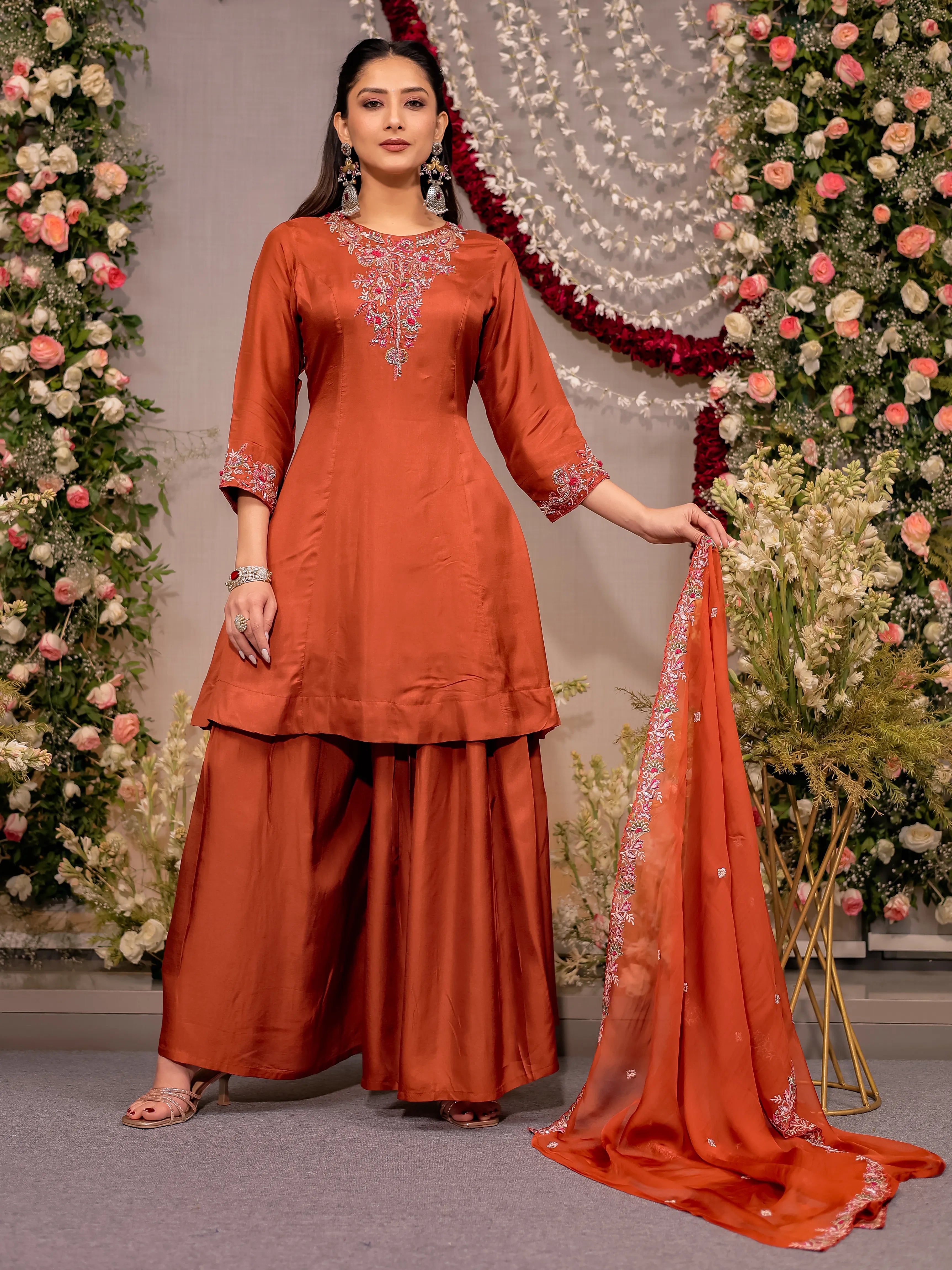 Woman in an orange traditional outfit with a matching dupatta against a decorated background
