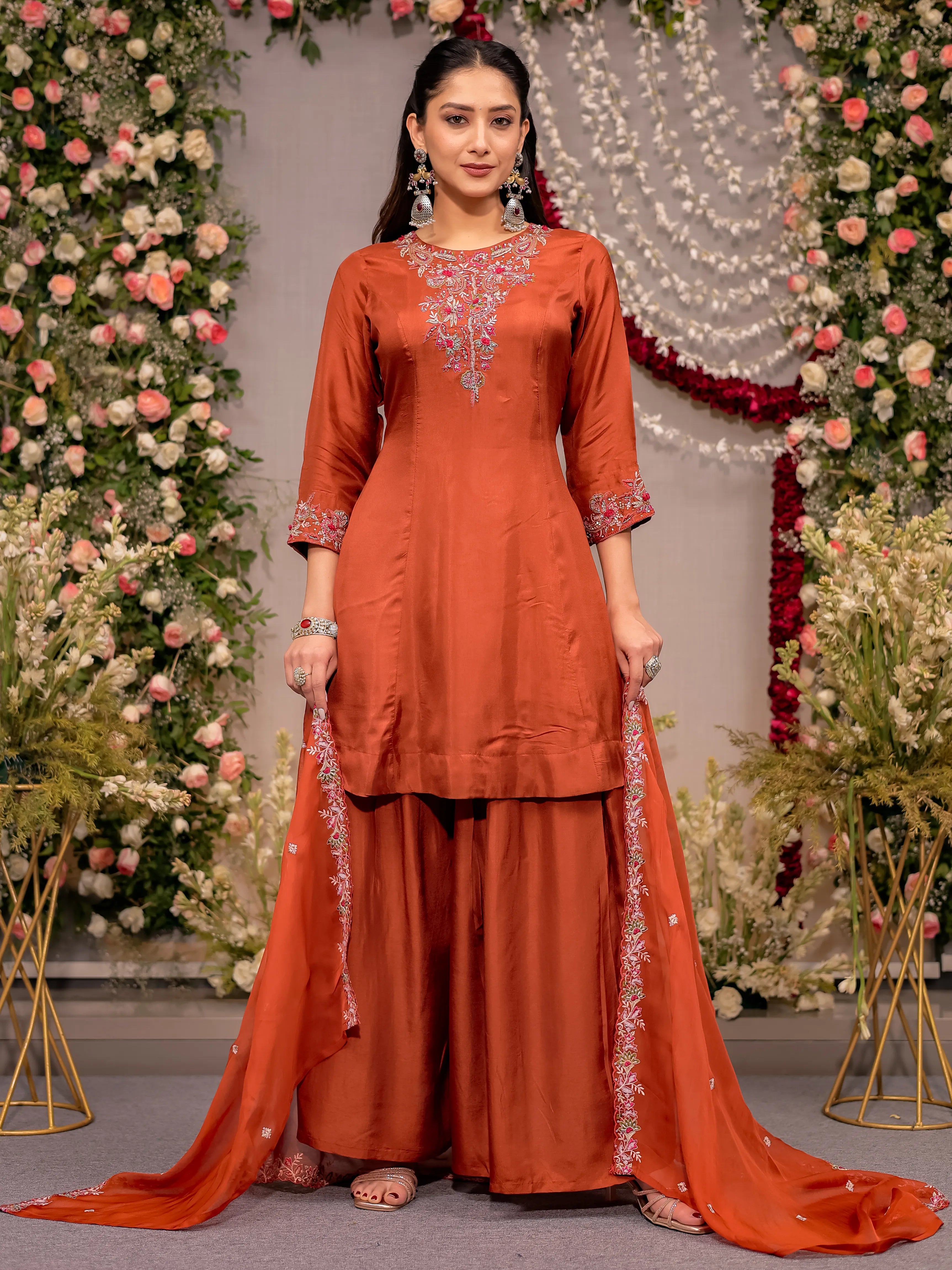 Woman wearing an orange traditional outfit with floral decorations in the background