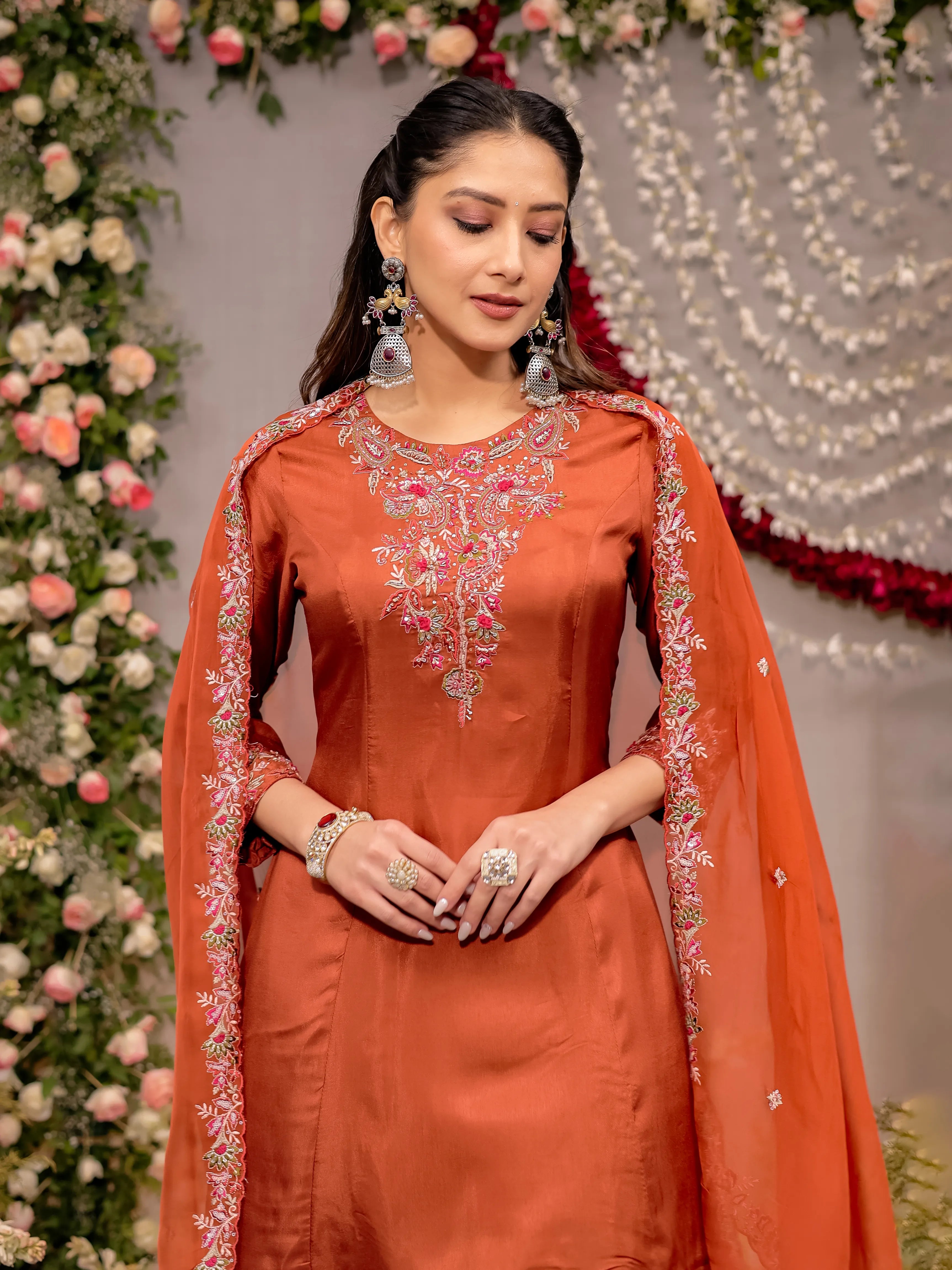 Woman in an orange traditional outfit with floral decorations in the background