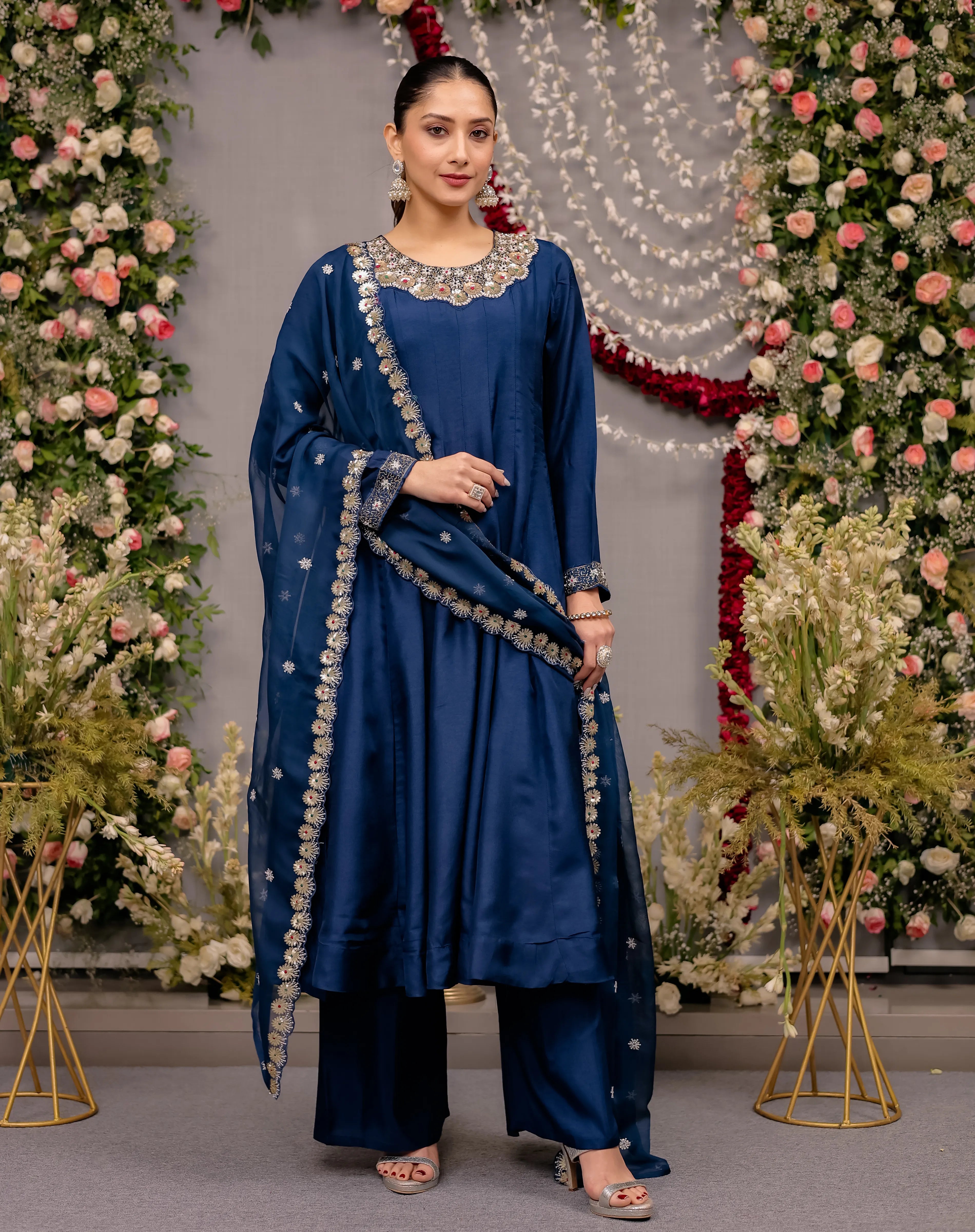 Woman in a blue traditional outfit standing in front of floral decorations