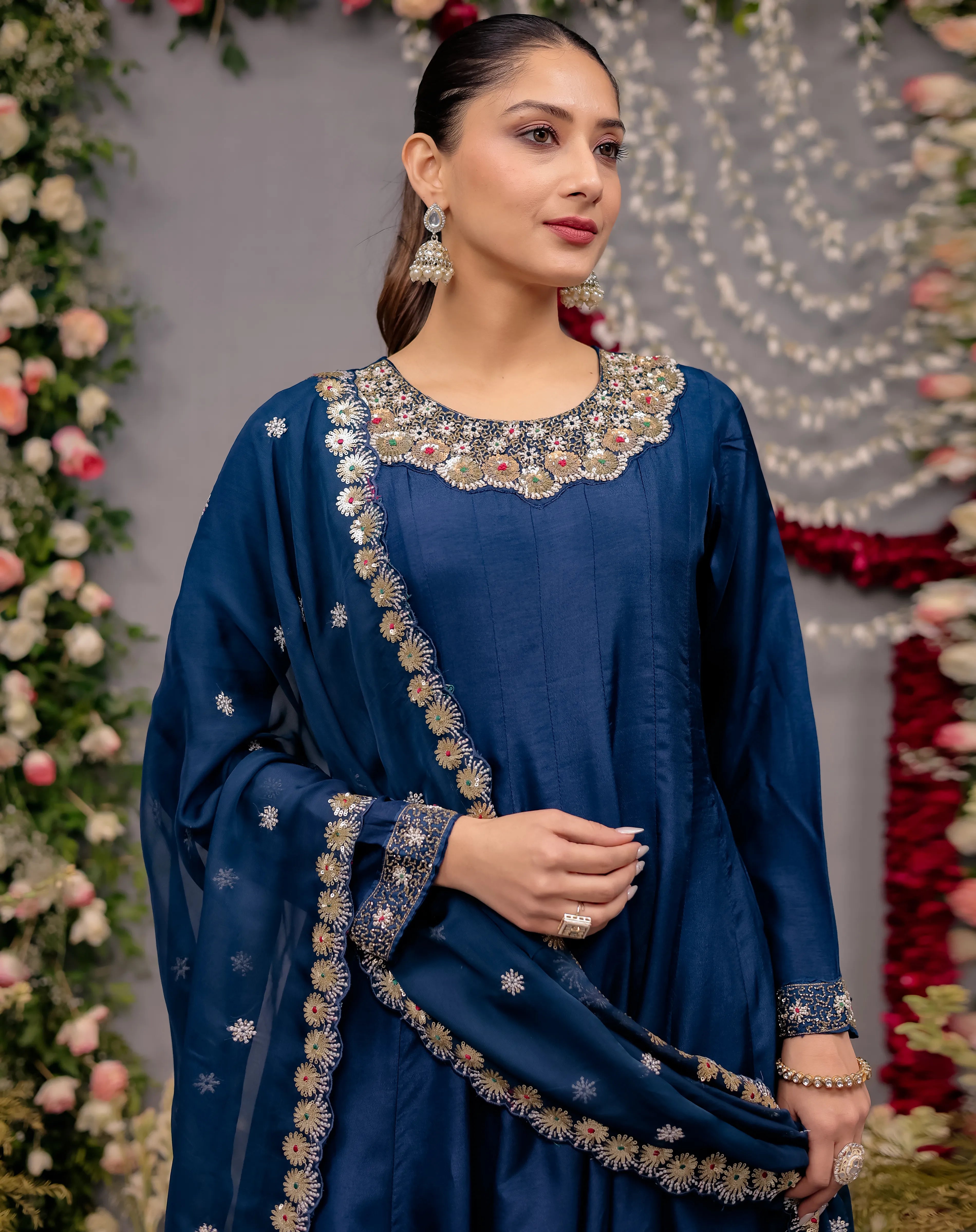 Woman wearing a blue embroidered traditional outfit with a floral decorated background