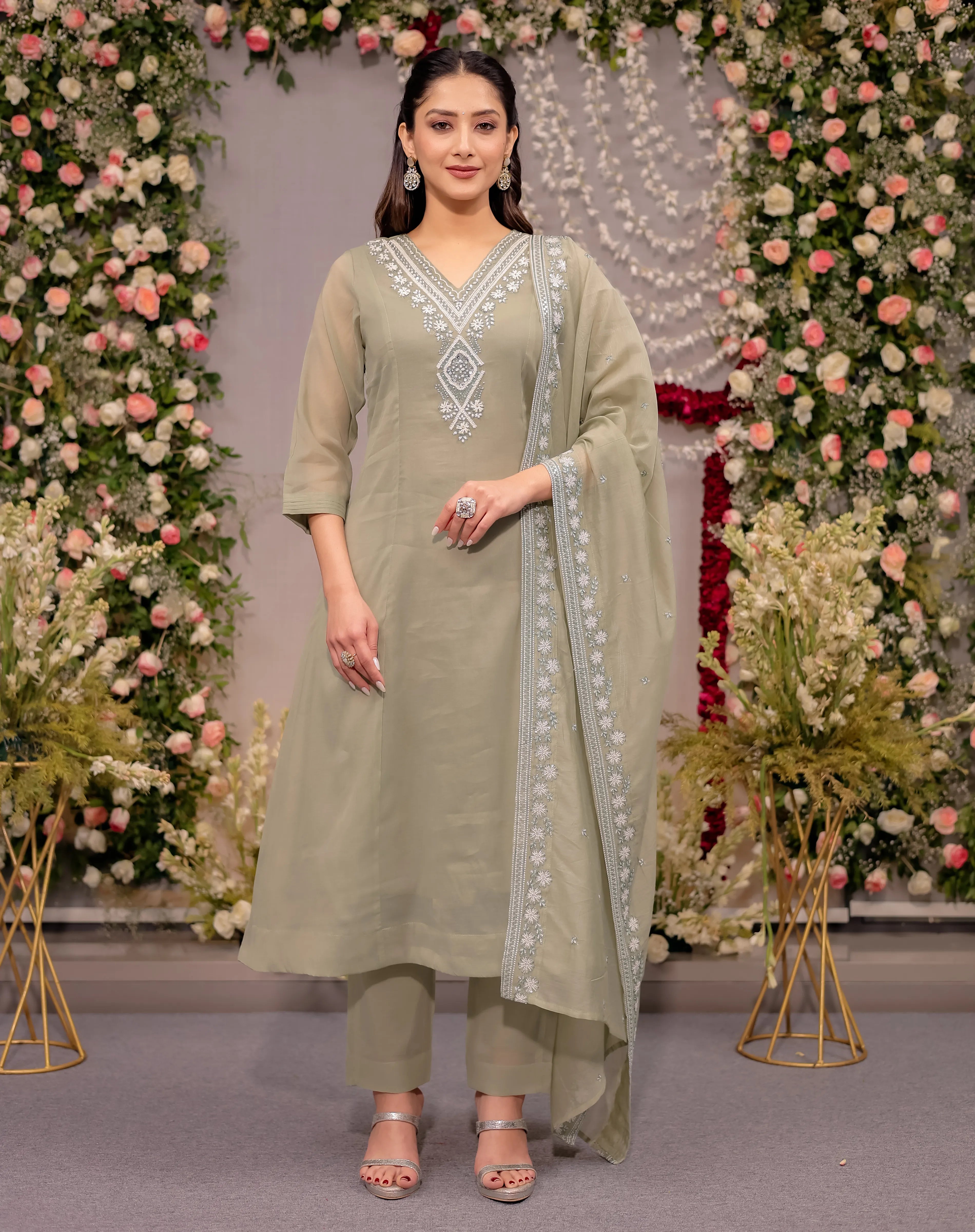 Woman in a light green traditional outfit with floral decorations in the background