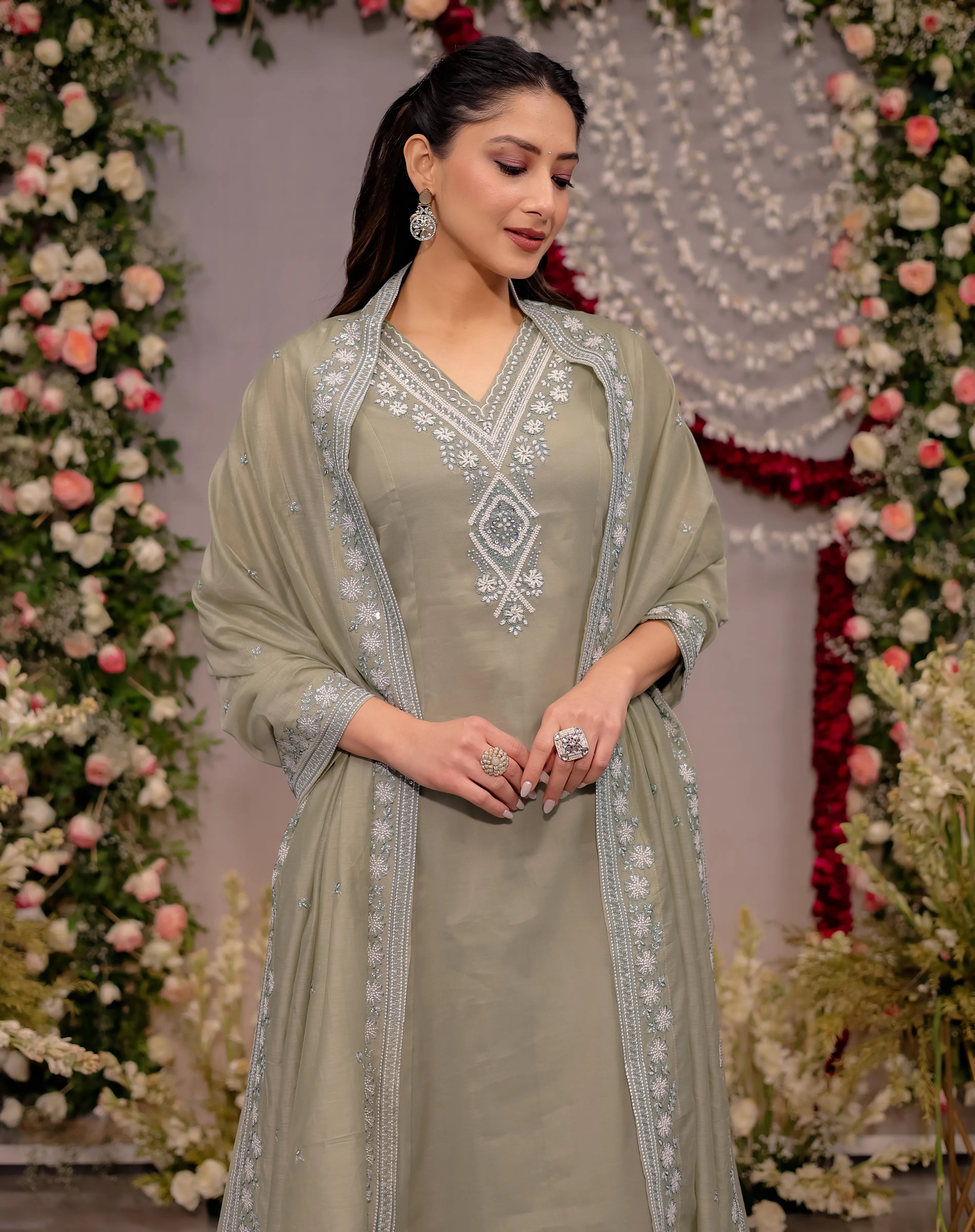 Woman in a light green traditional outfit with silver embroidery against a decorated floral background