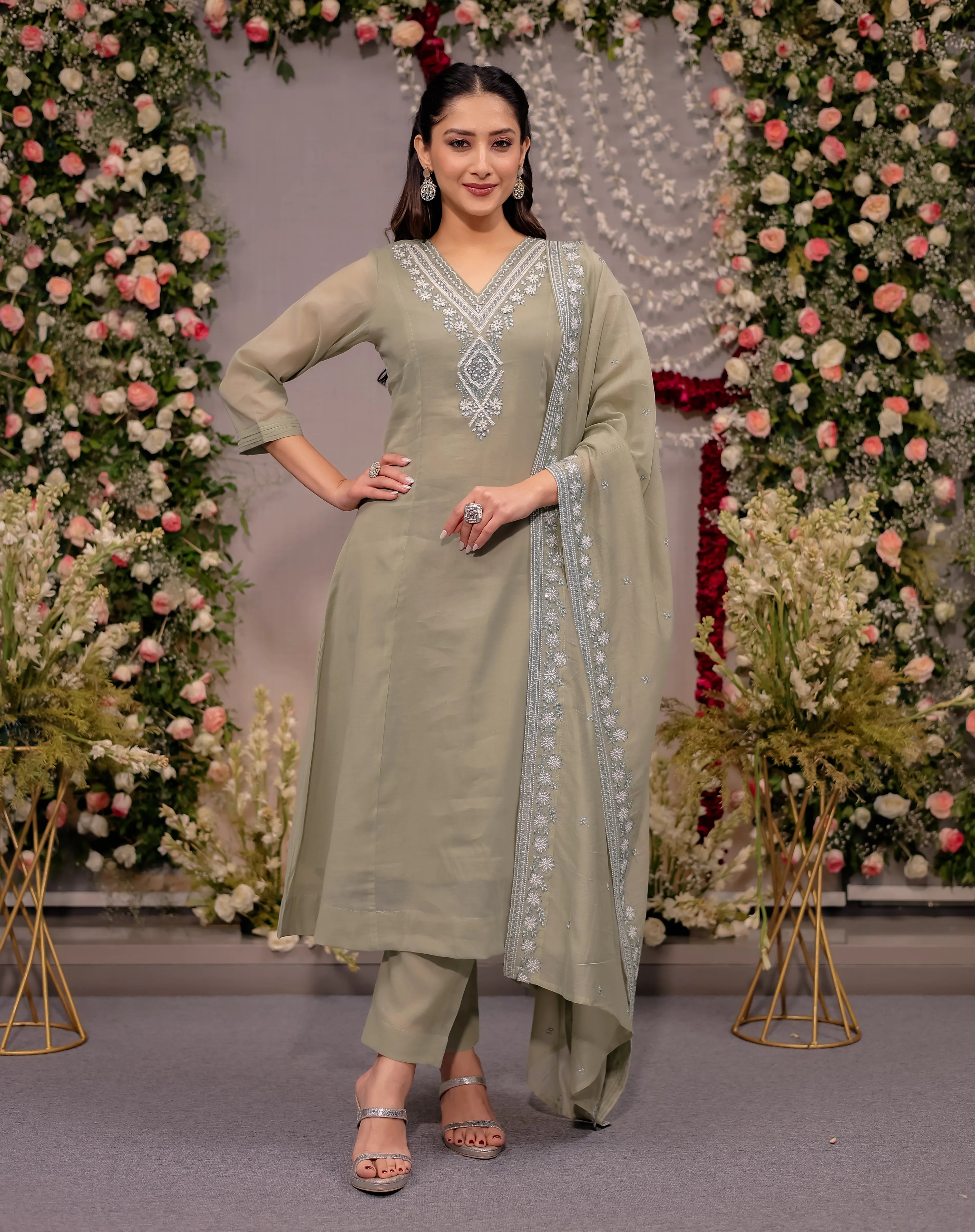 Woman in a green traditional outfit with floral decorations in the background