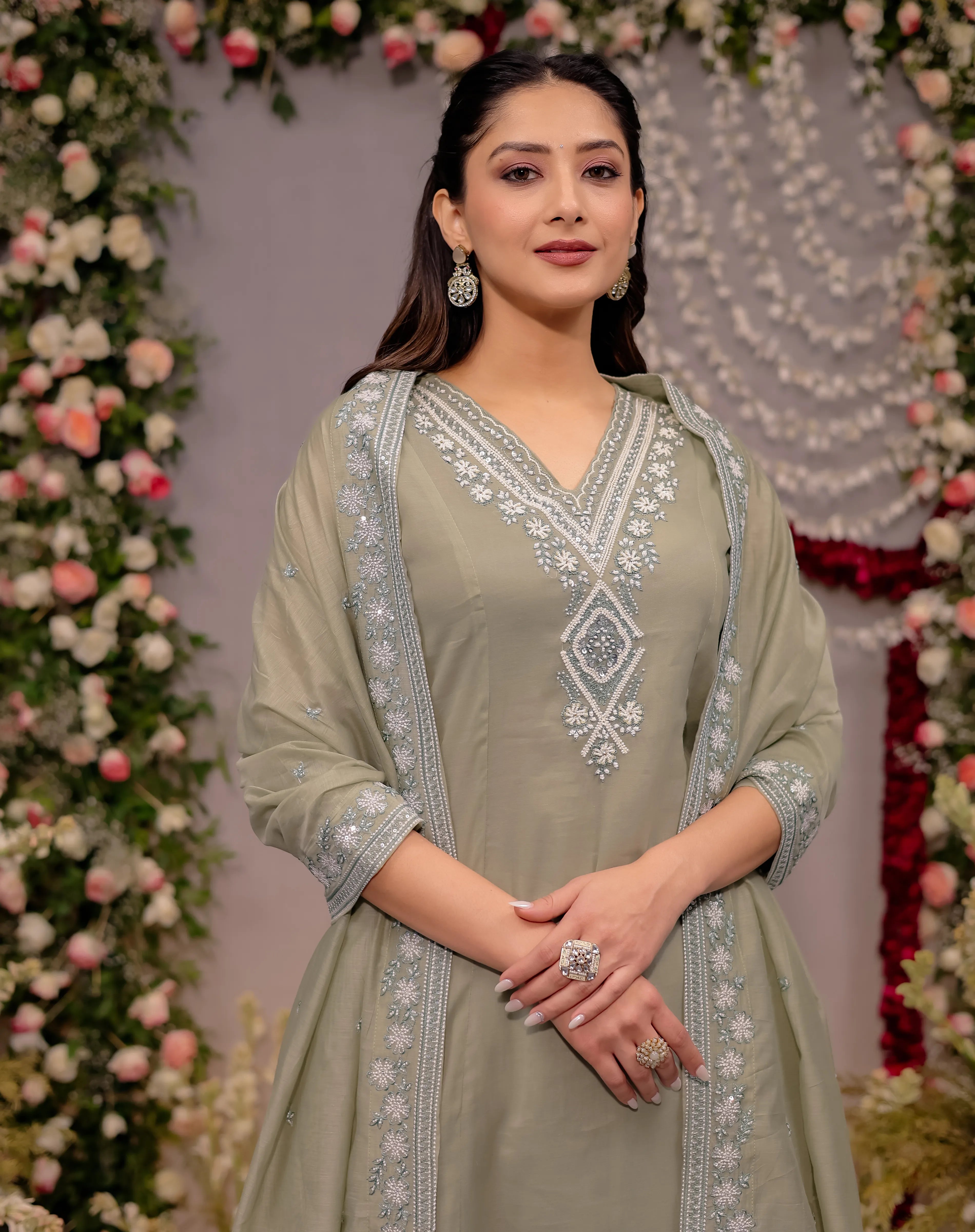 Woman in a light green embroidered outfit standing in front of floral decorations