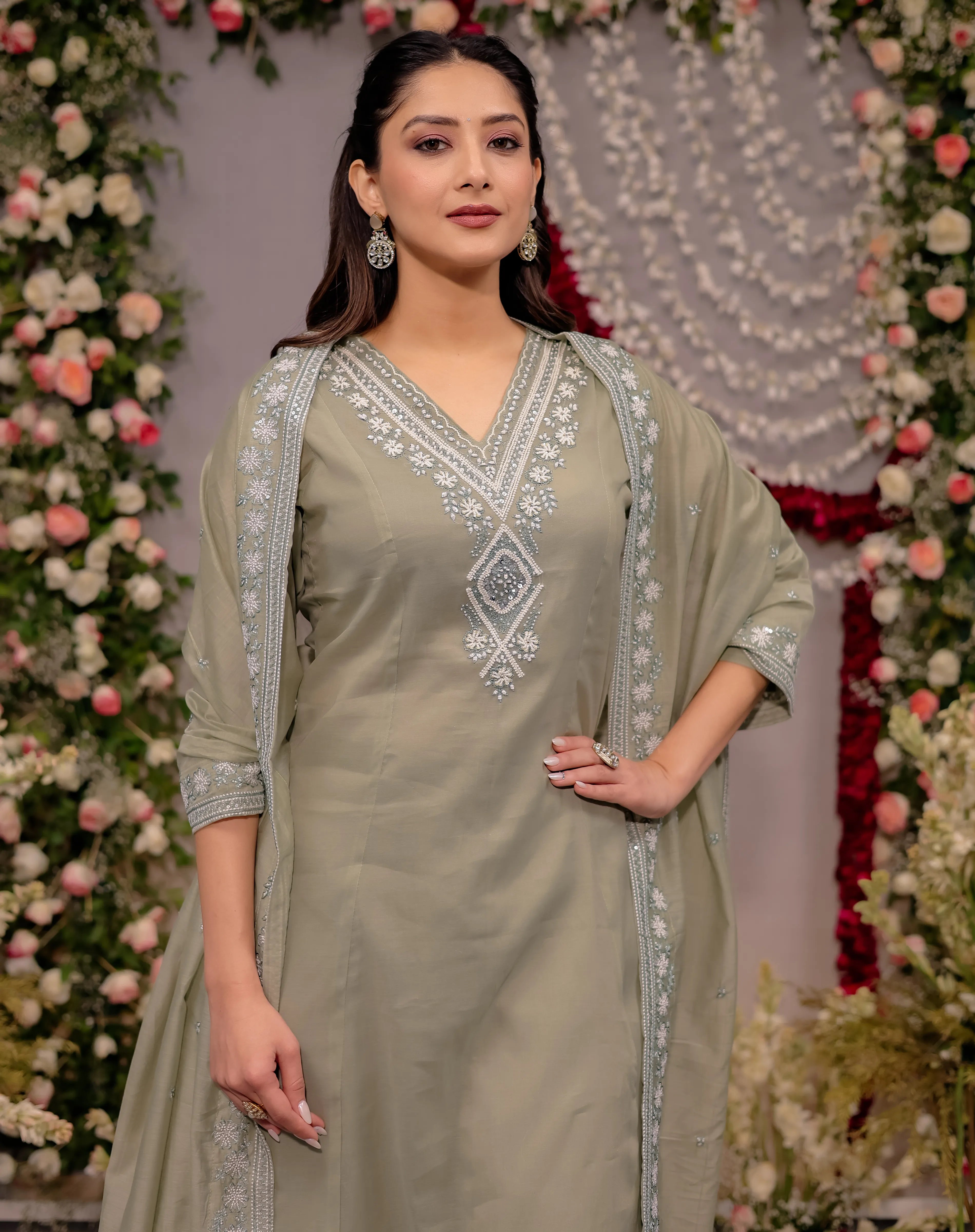 Woman in a light green traditional outfit with silver embroidery against a floral decorated background