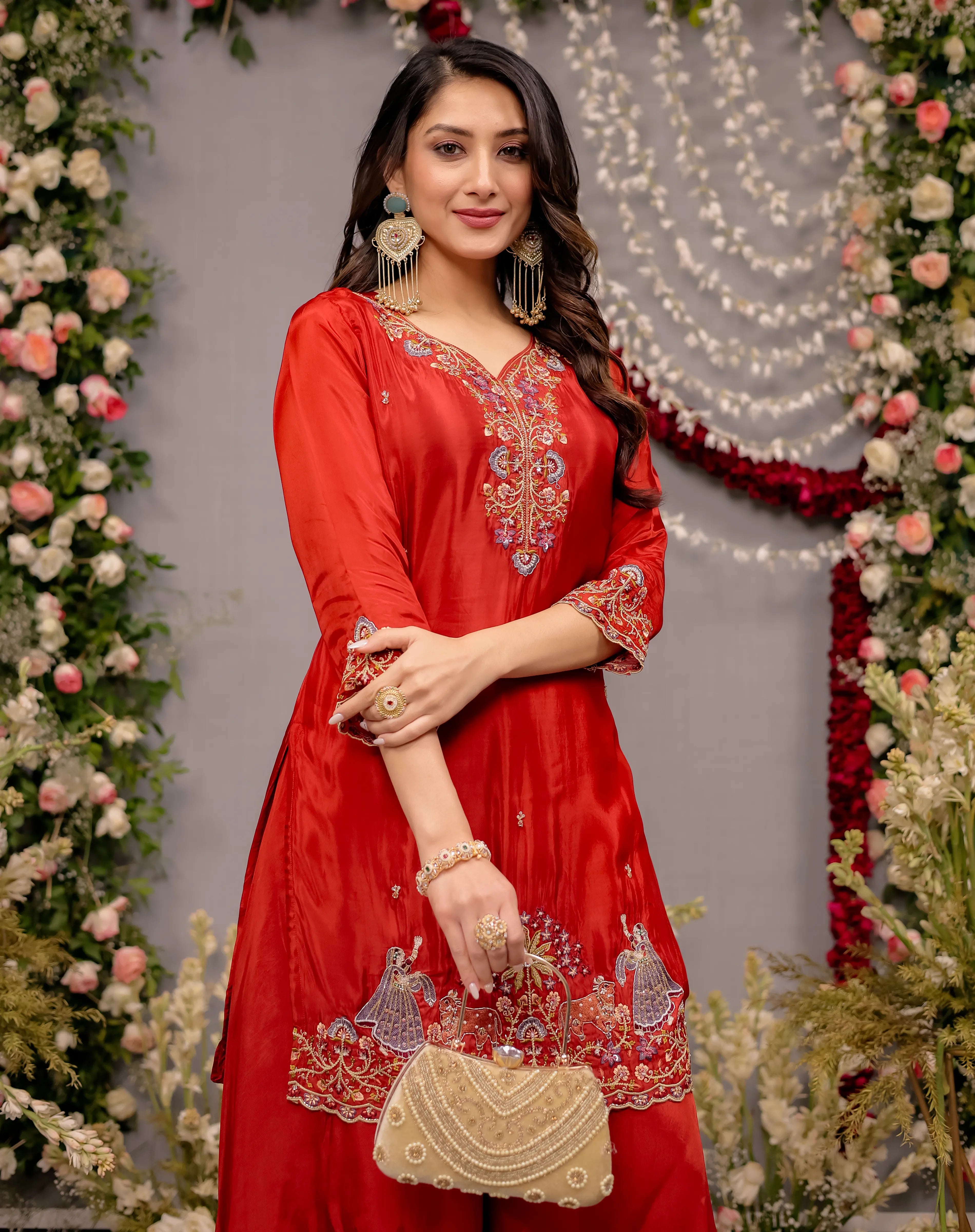 Woman in a red embroidered dress holding a gold purse against a decorated background