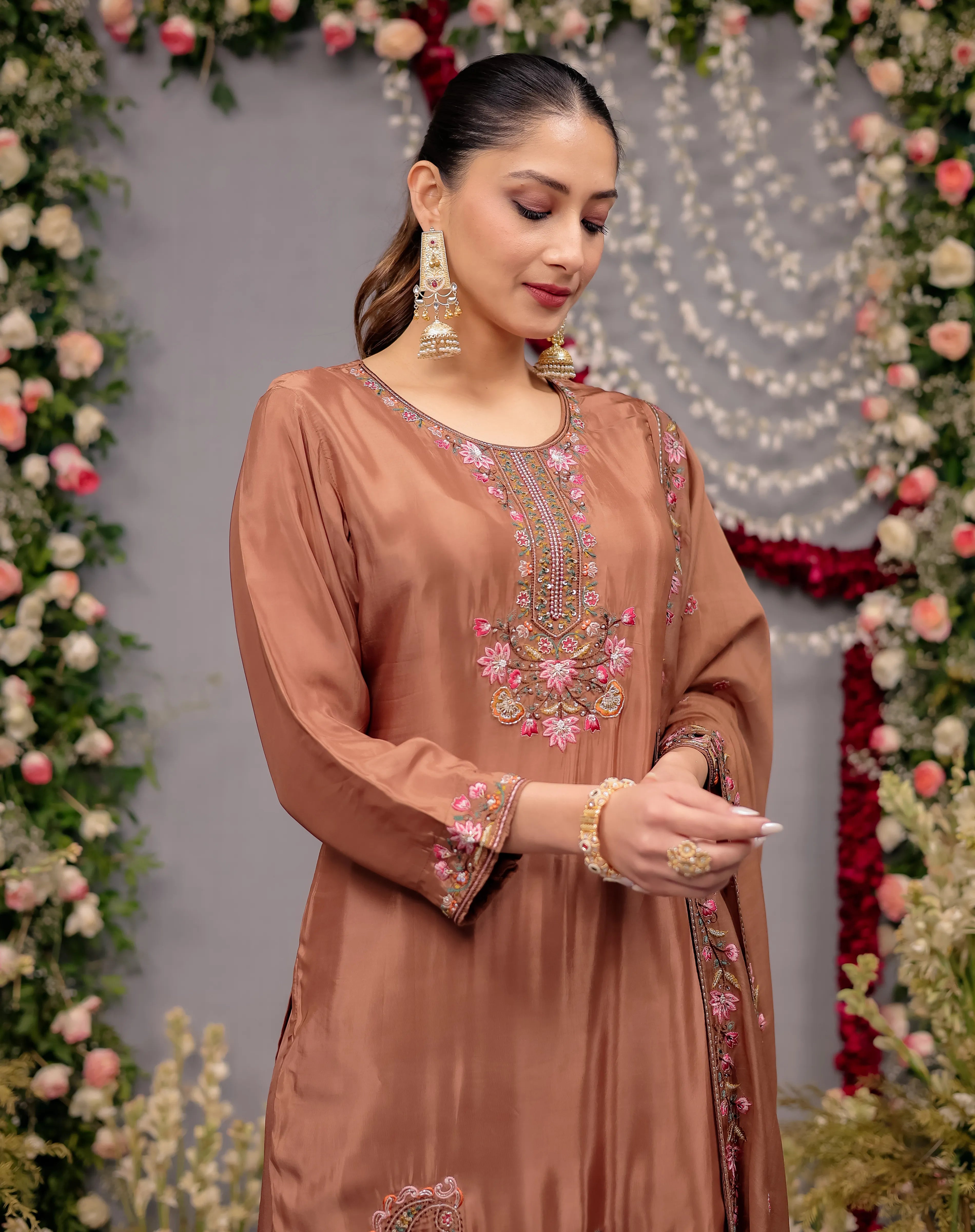 Woman wearing a brown embroidered dress in front of floral decorations
