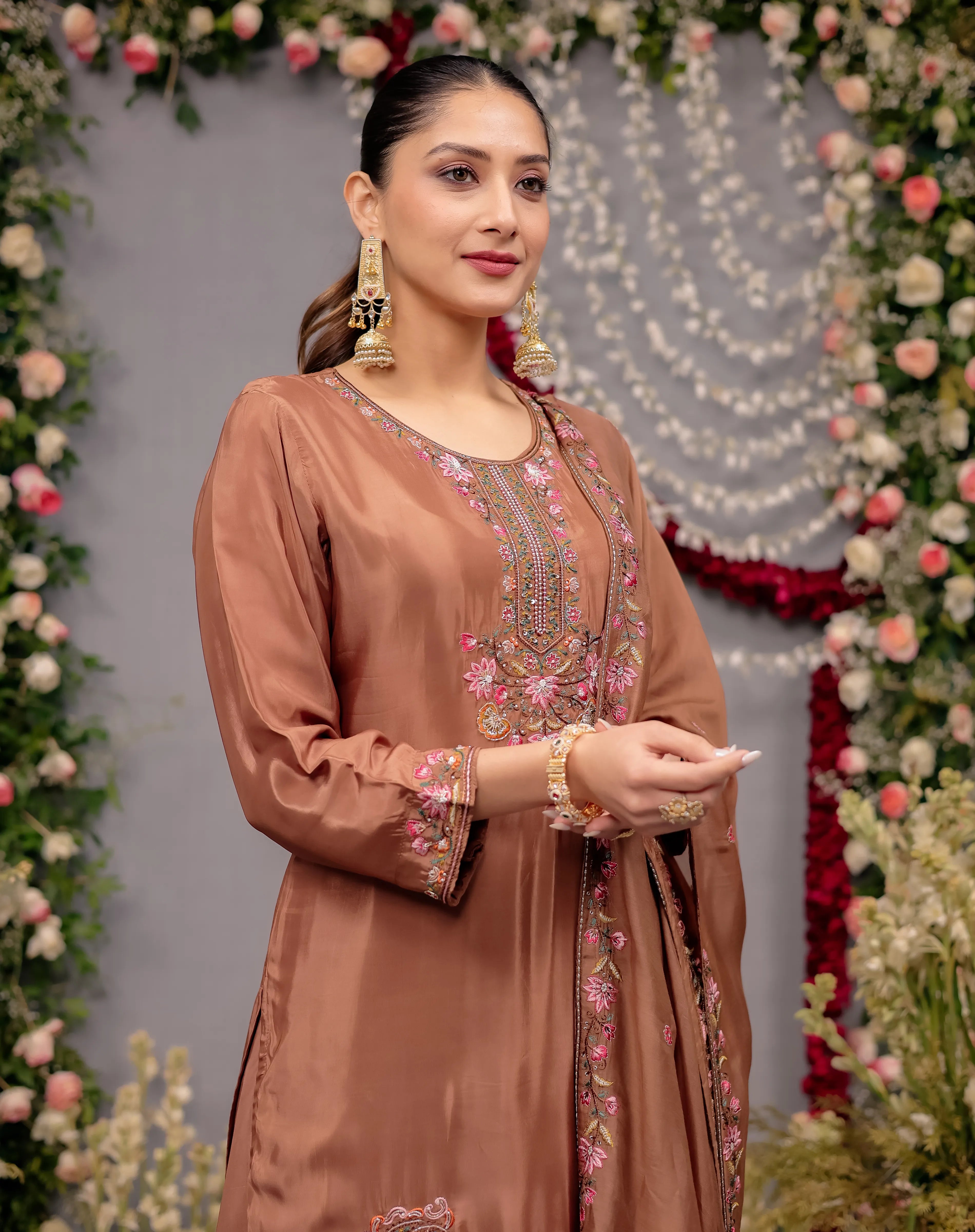 Woman in a brown embroidered outfit standing in front of floral decorations
