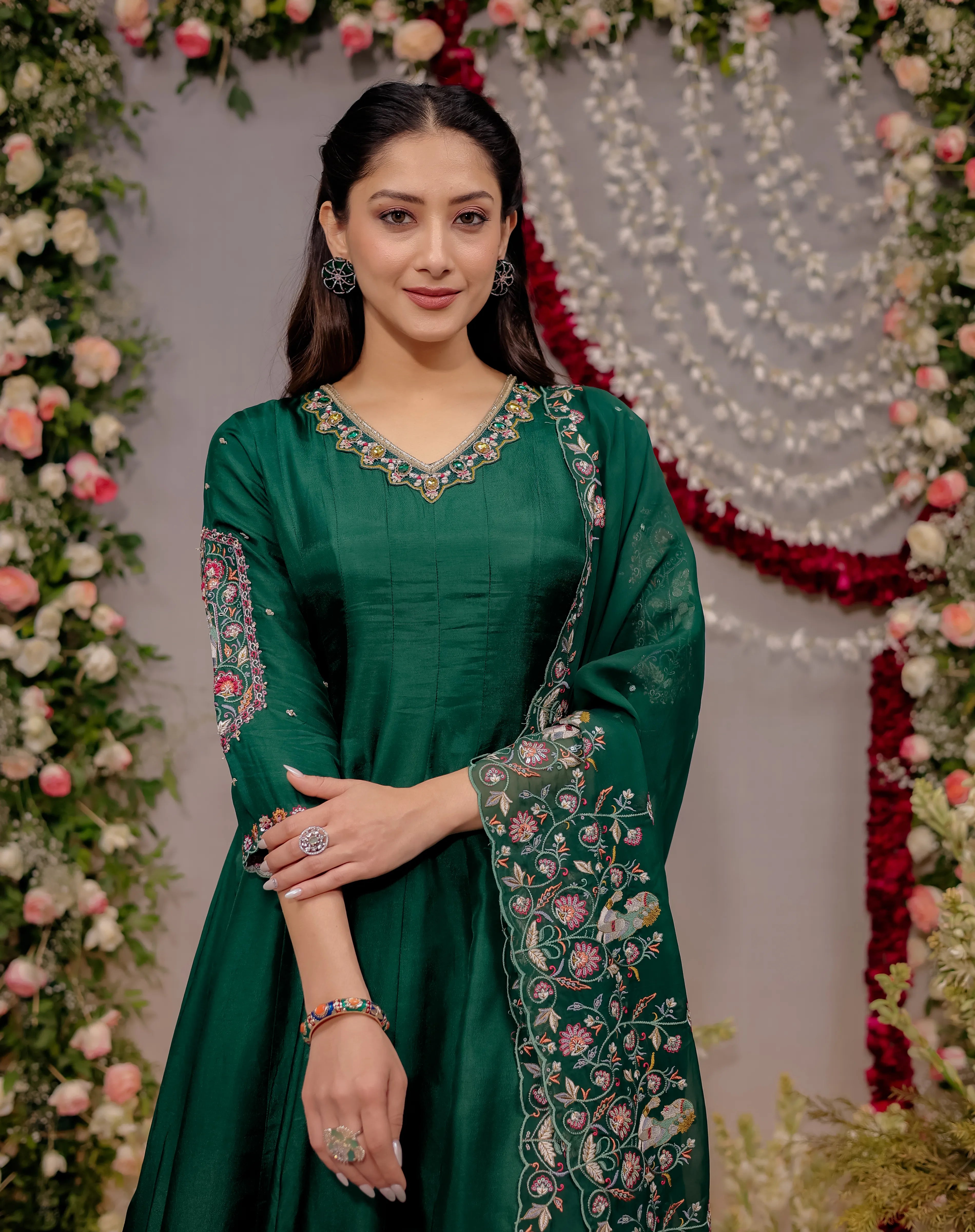 Woman in a green traditional outfit with floral patterns against a decorated background
