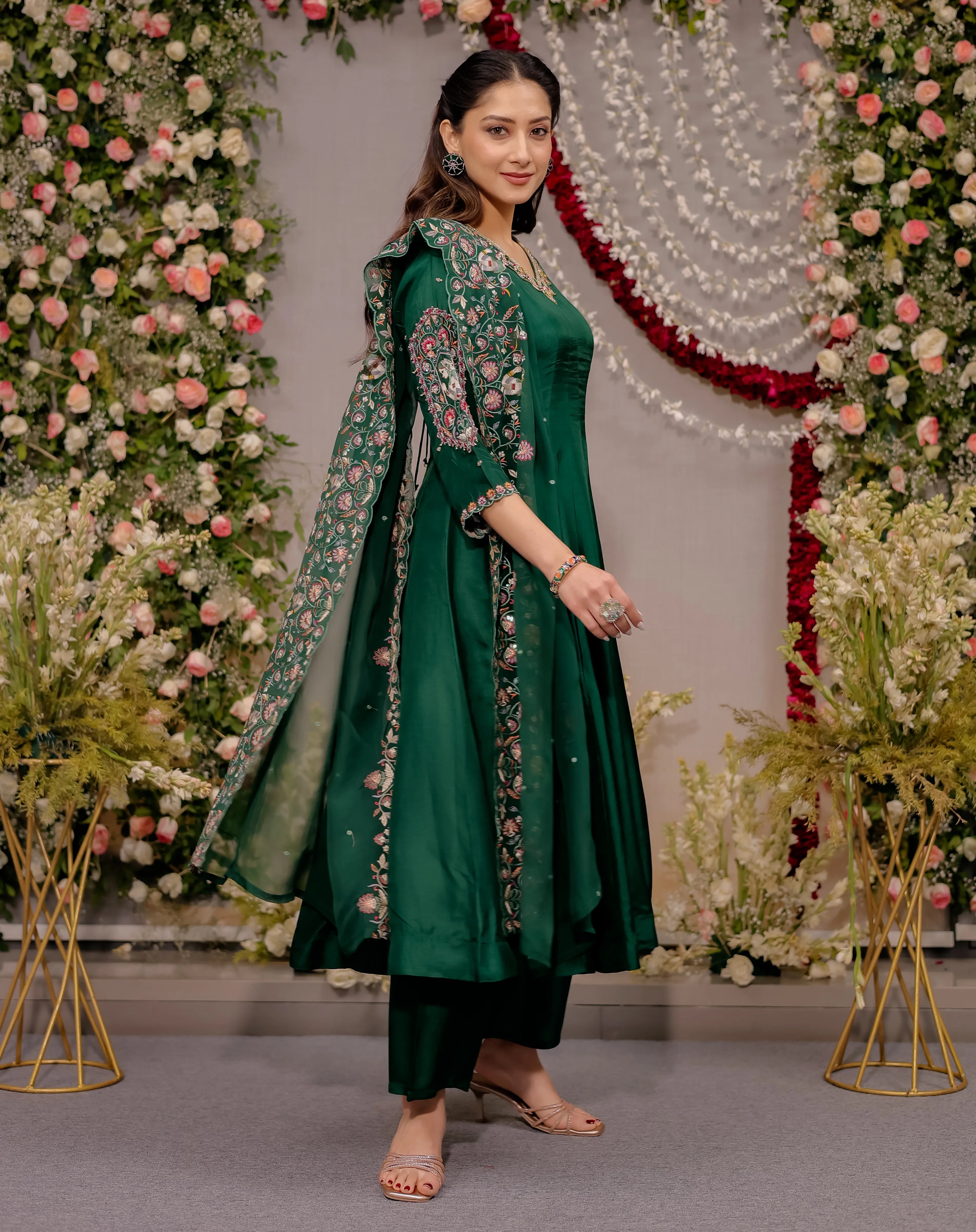 Woman in a green traditional outfit standing in front of floral decorations