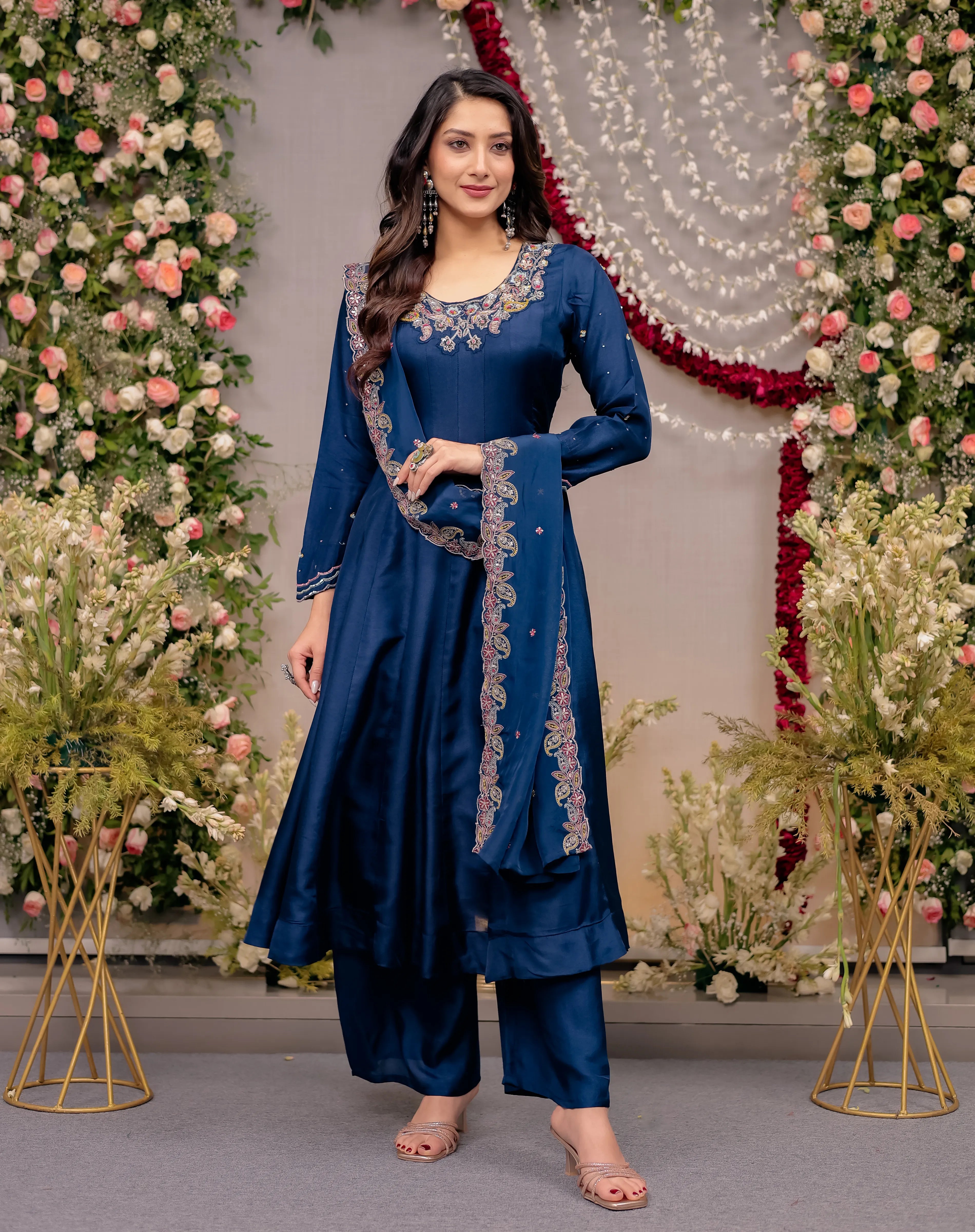 Woman in a blue traditional outfit standing in front of floral decorations