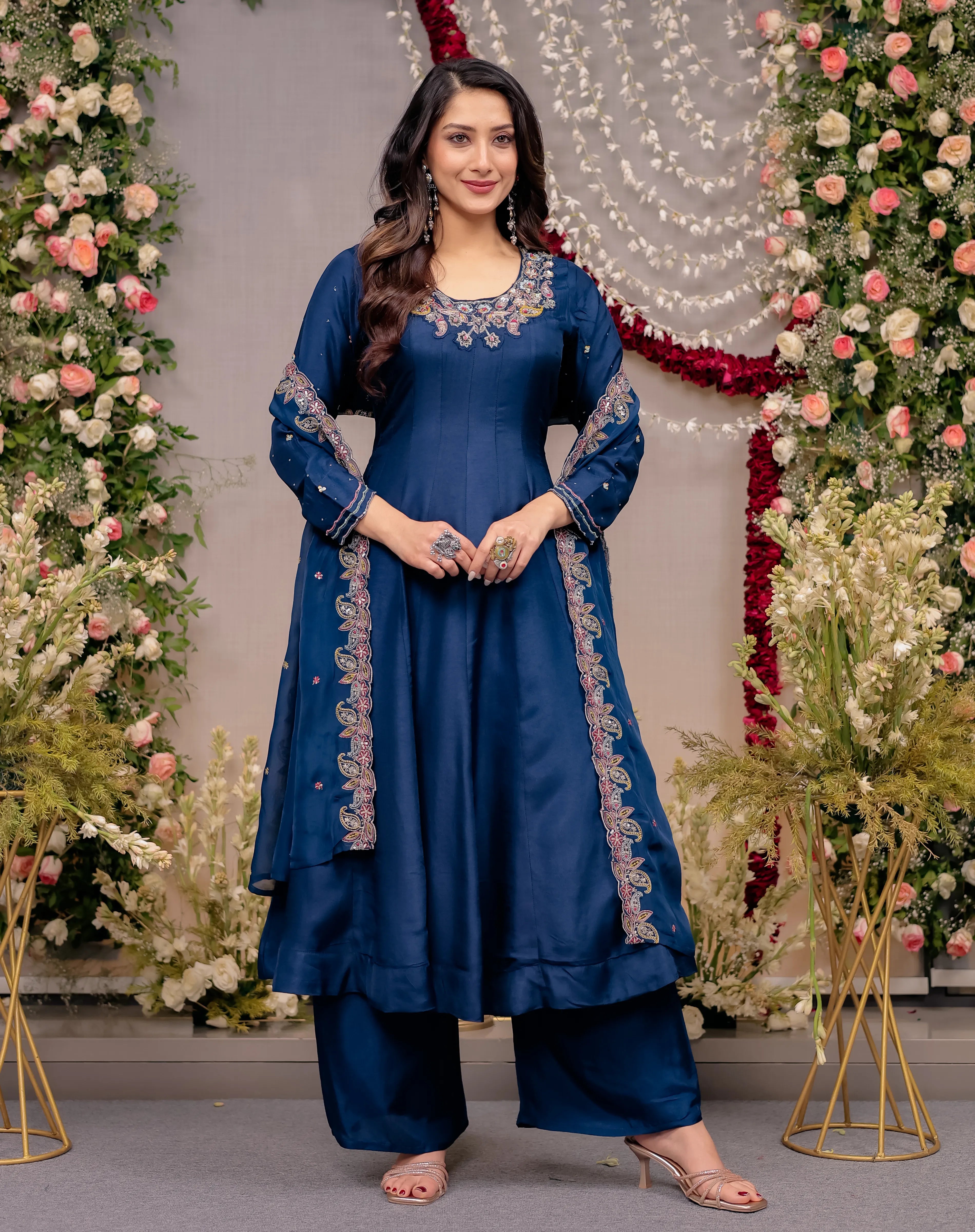 Woman in a blue traditional outfit standing in front of floral decorations
