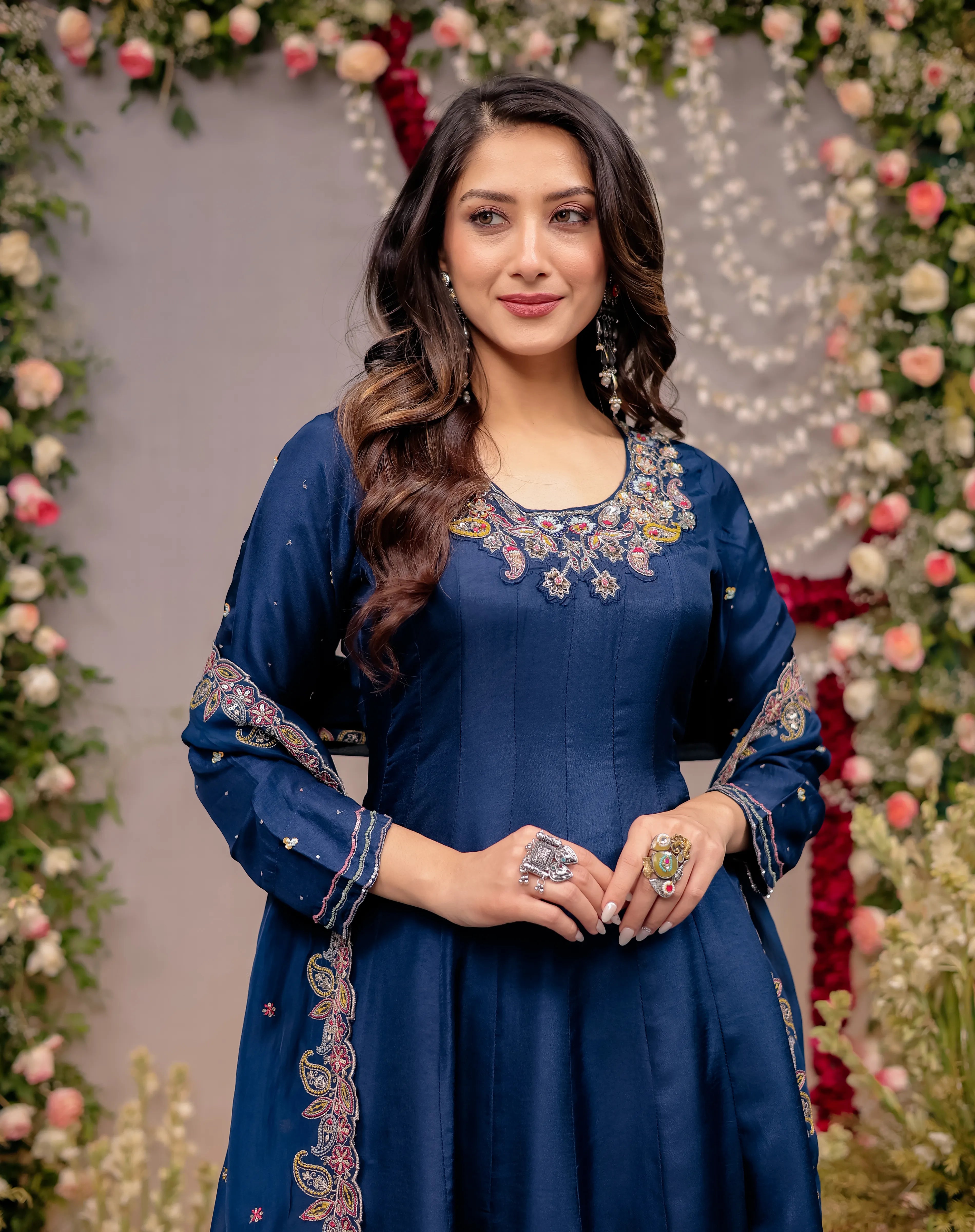 Woman in a blue embroidered dress standing in front of floral decorations