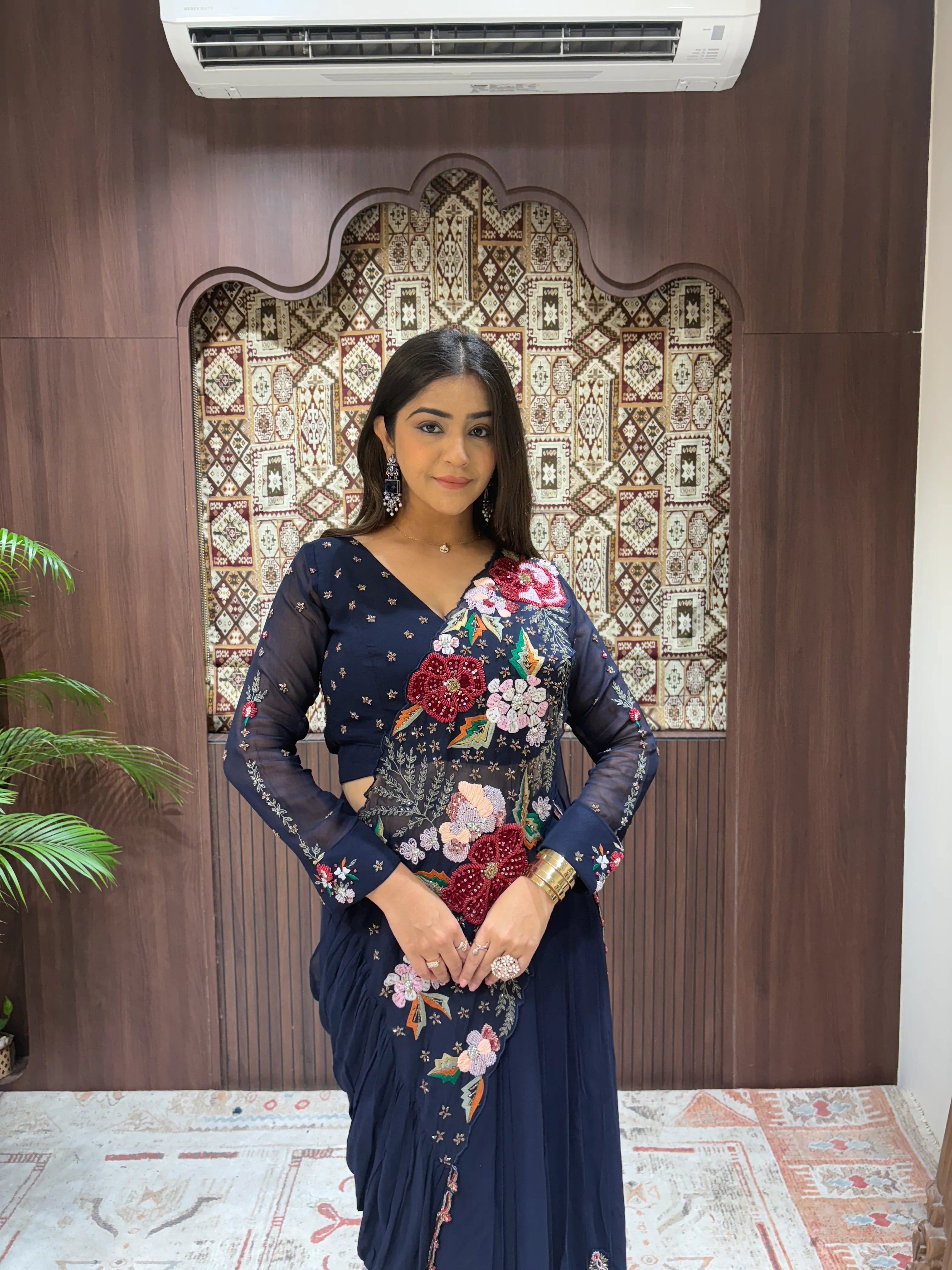 Woman in a floral saree standing in front of a decorative wall.