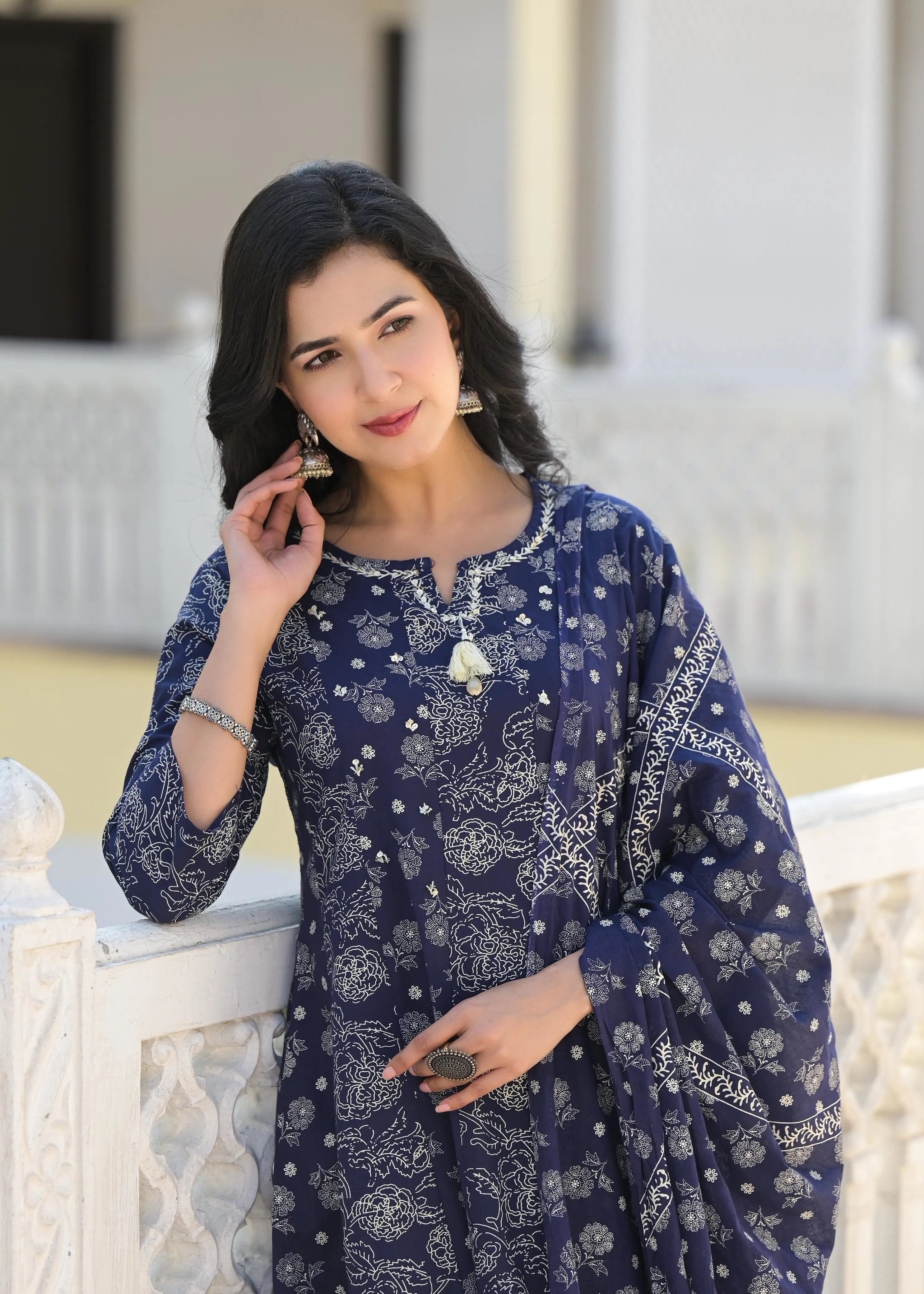 Woman wearing a blue traditional outfit with white patterns, standing outdoors.