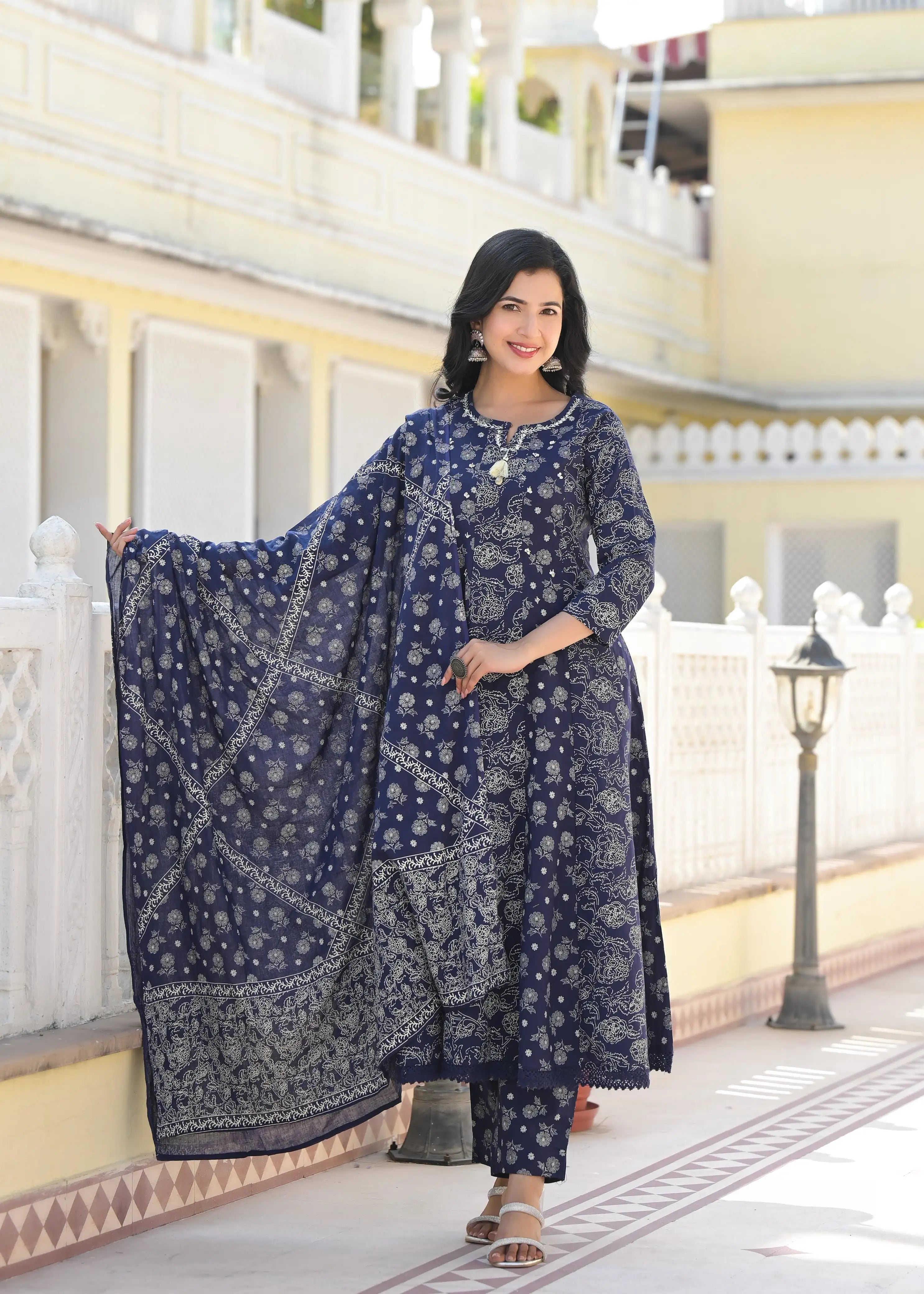 Woman in a blue traditional outfit with a matching dupatta standing on a decorative porch.