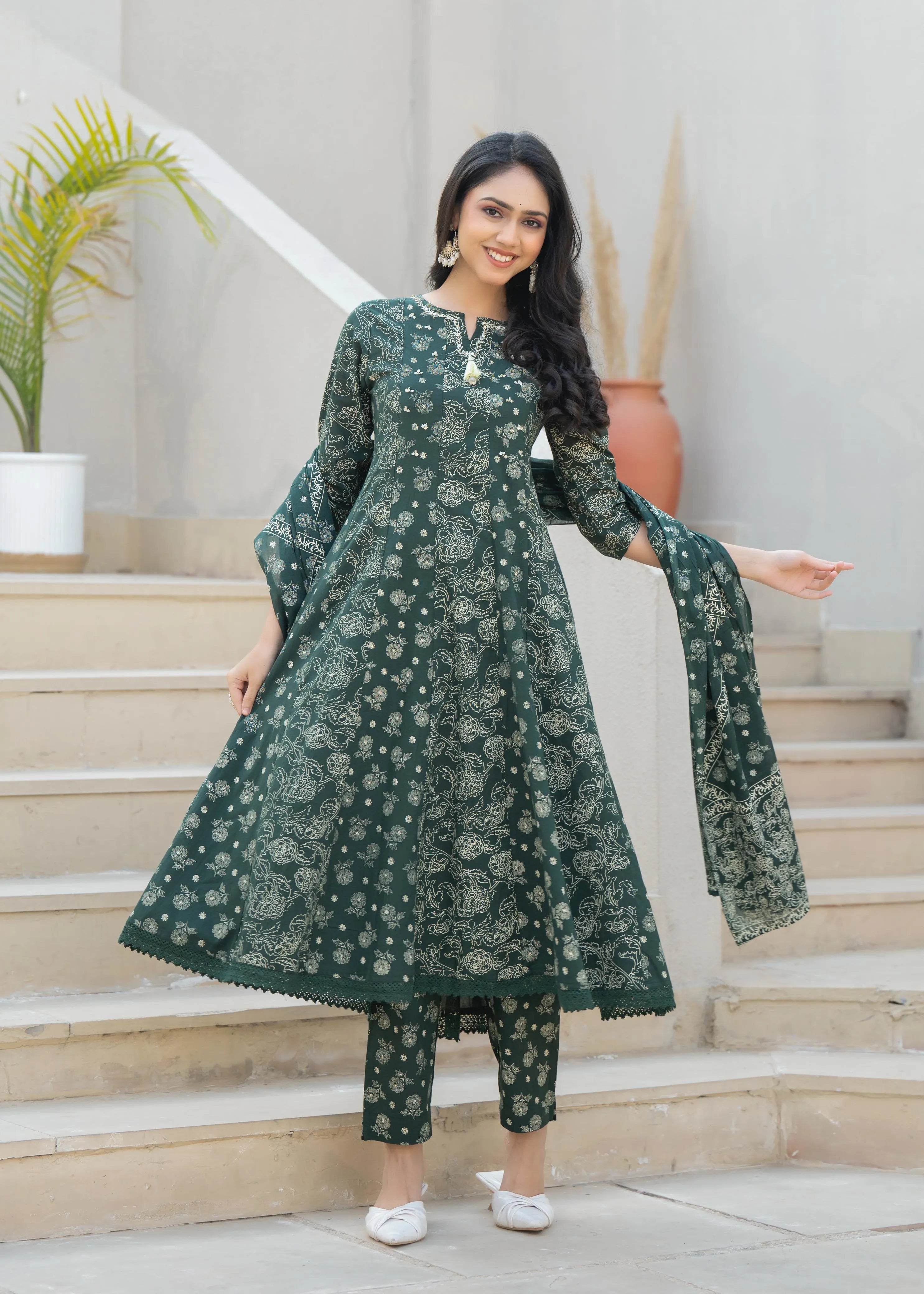 Woman wearing a green floral outfit standing on steps with plants in the background