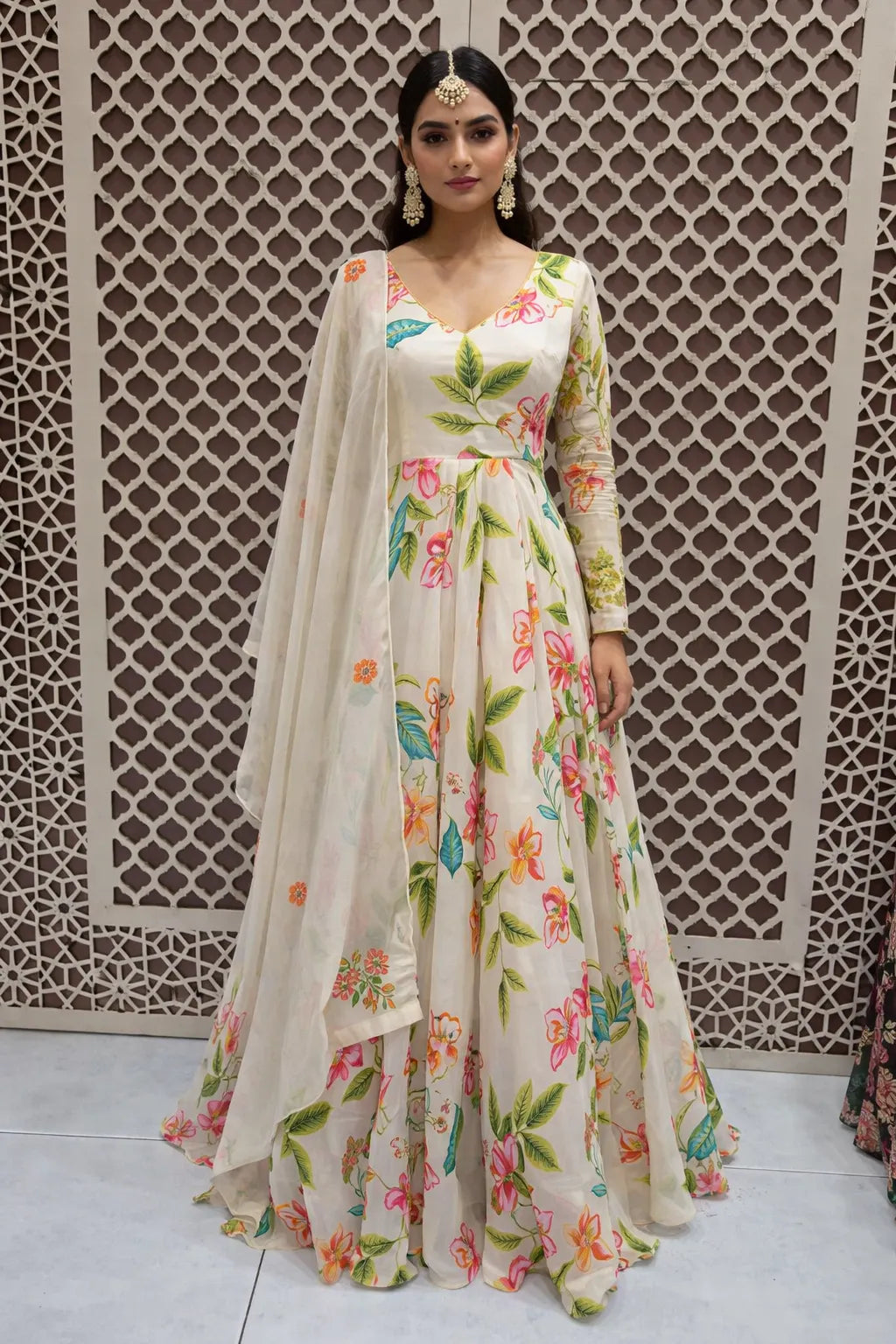Woman wearing a floral dress with a matching dupatta against an intricate lattice background