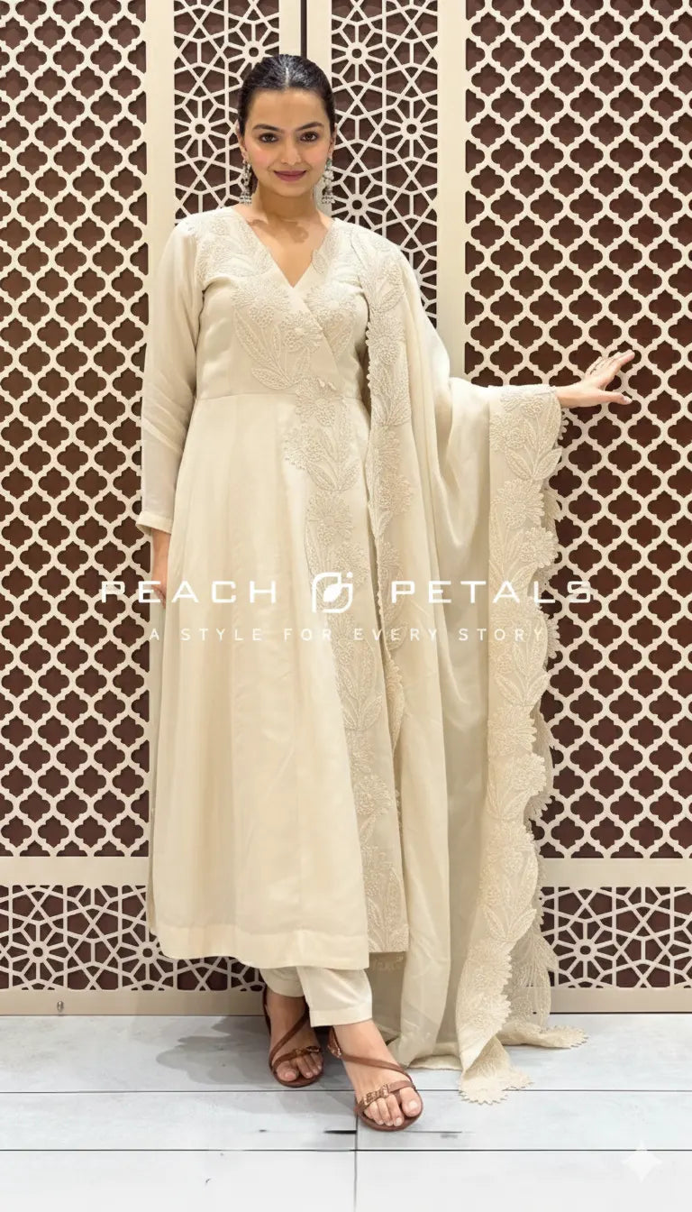 Woman in a beige traditional outfit with a patterned wall background, featuring the brand 'Peach Petals'.