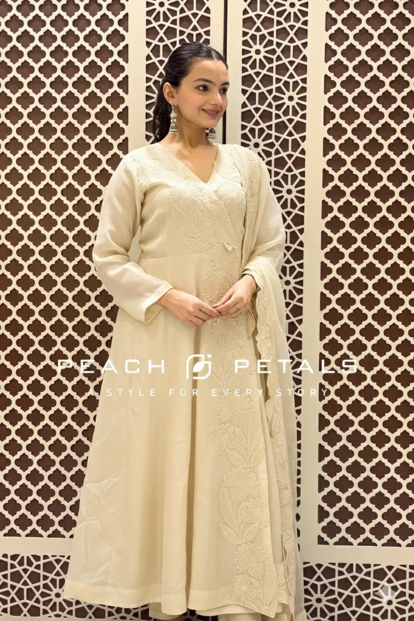 Woman in a beige traditional outfit standing against a decorative wall with 'Peach Petals' branding.