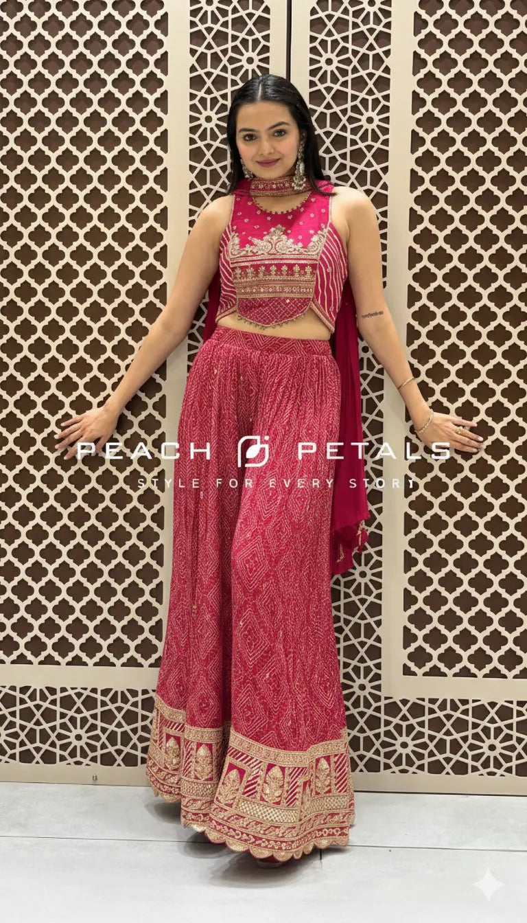 Woman in a pink traditional outfit with intricate designs against a decorative wall.
