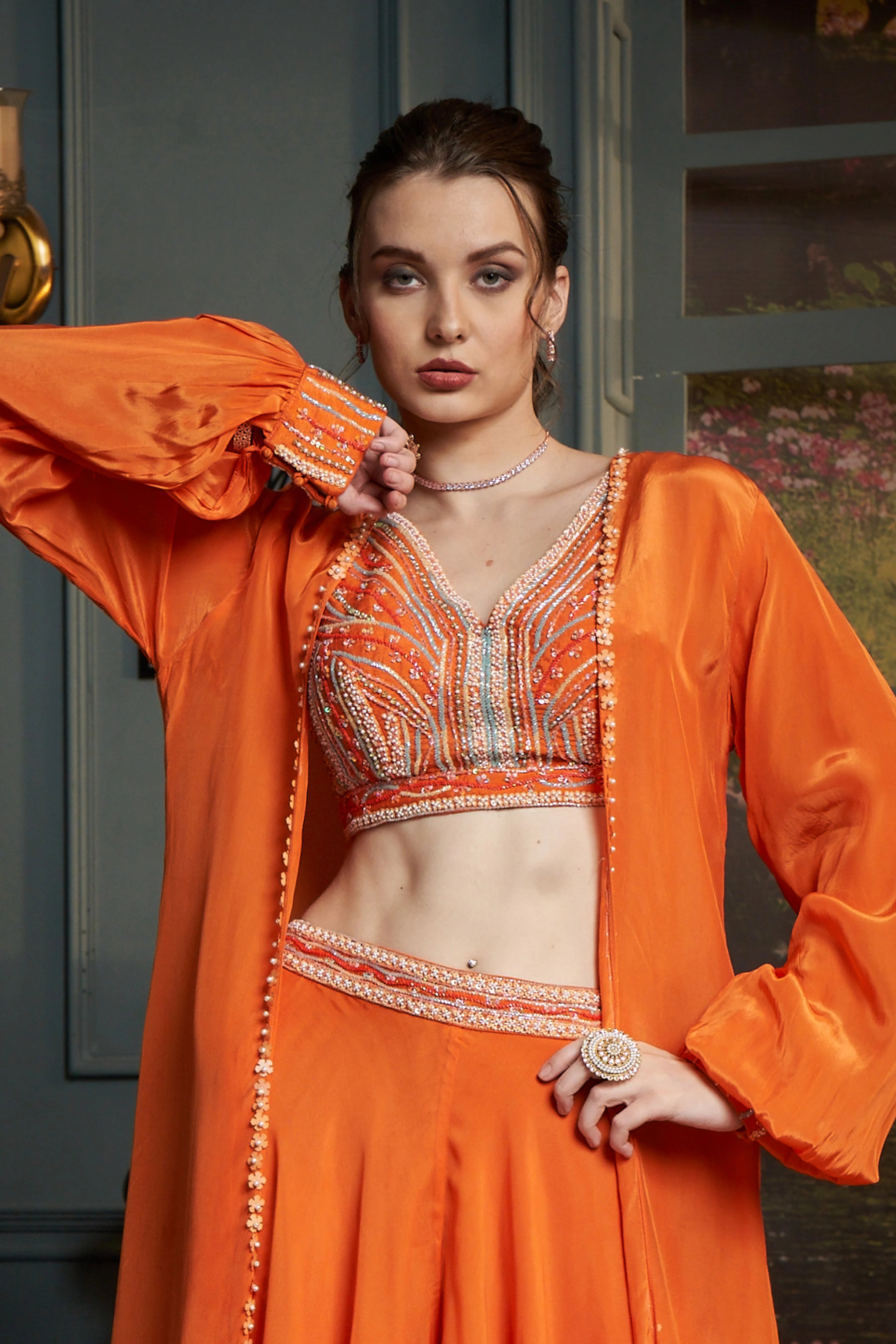 Vibrant orange ensemble featuring a heavily embellished crop top, matching flared Palazzo Set, and a long-sleeved cape.